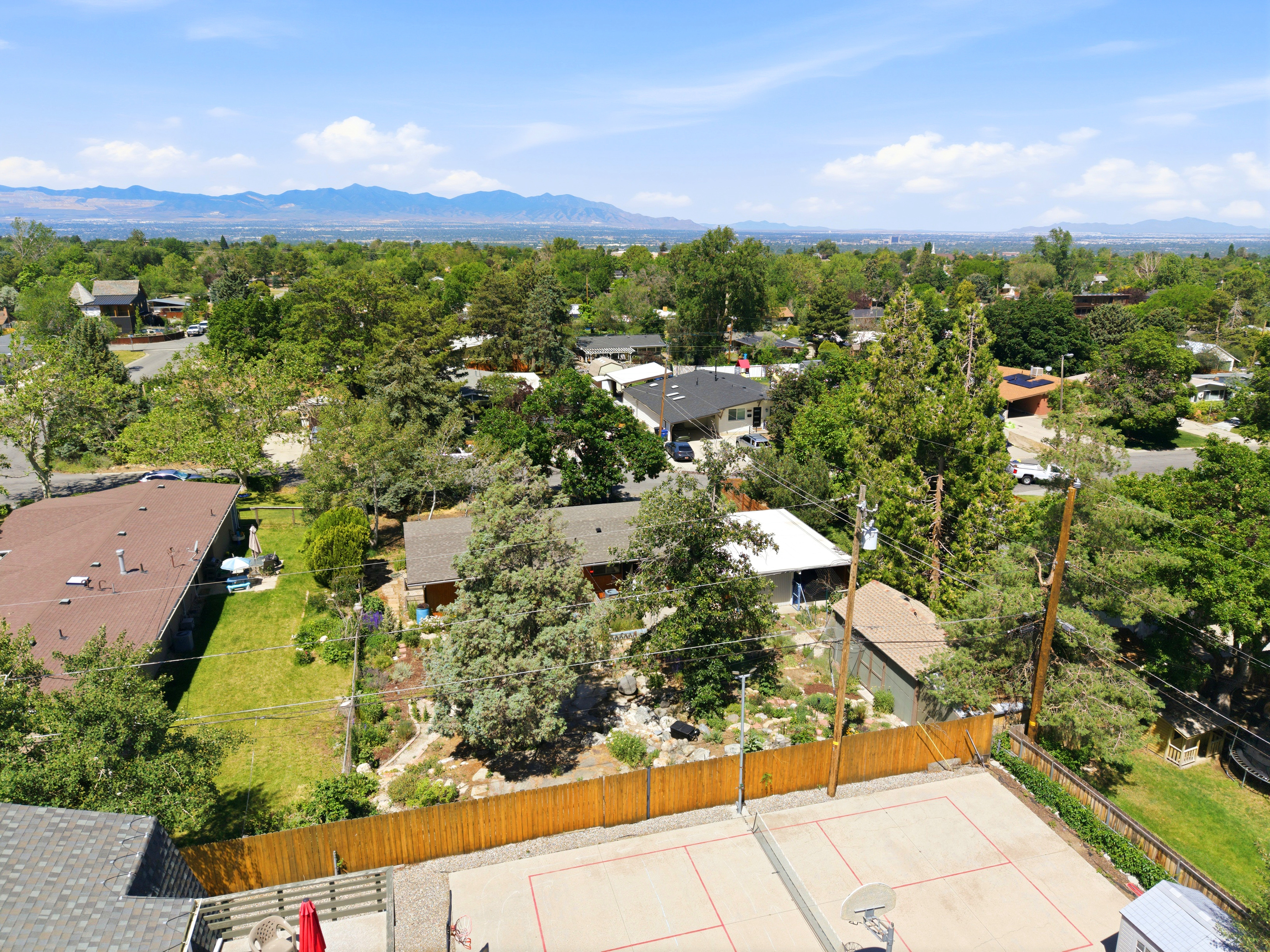 Aerial perspective showcasing a concrete sport court with perimeter fencing, surrounded by mature trees