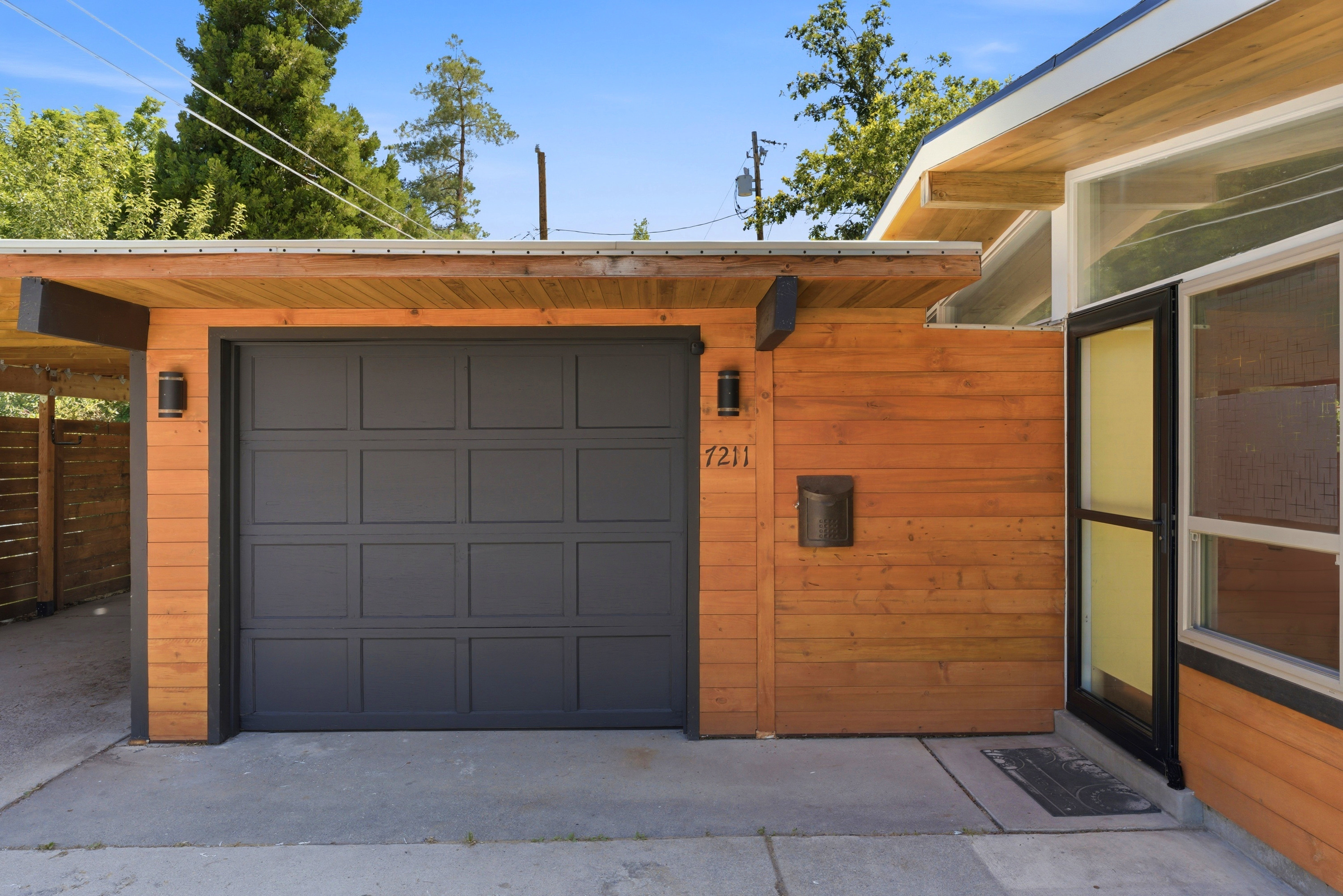 Modern exterior featuring horizontal wood-finish siding, a dark gray garage door, and a covered entryway
