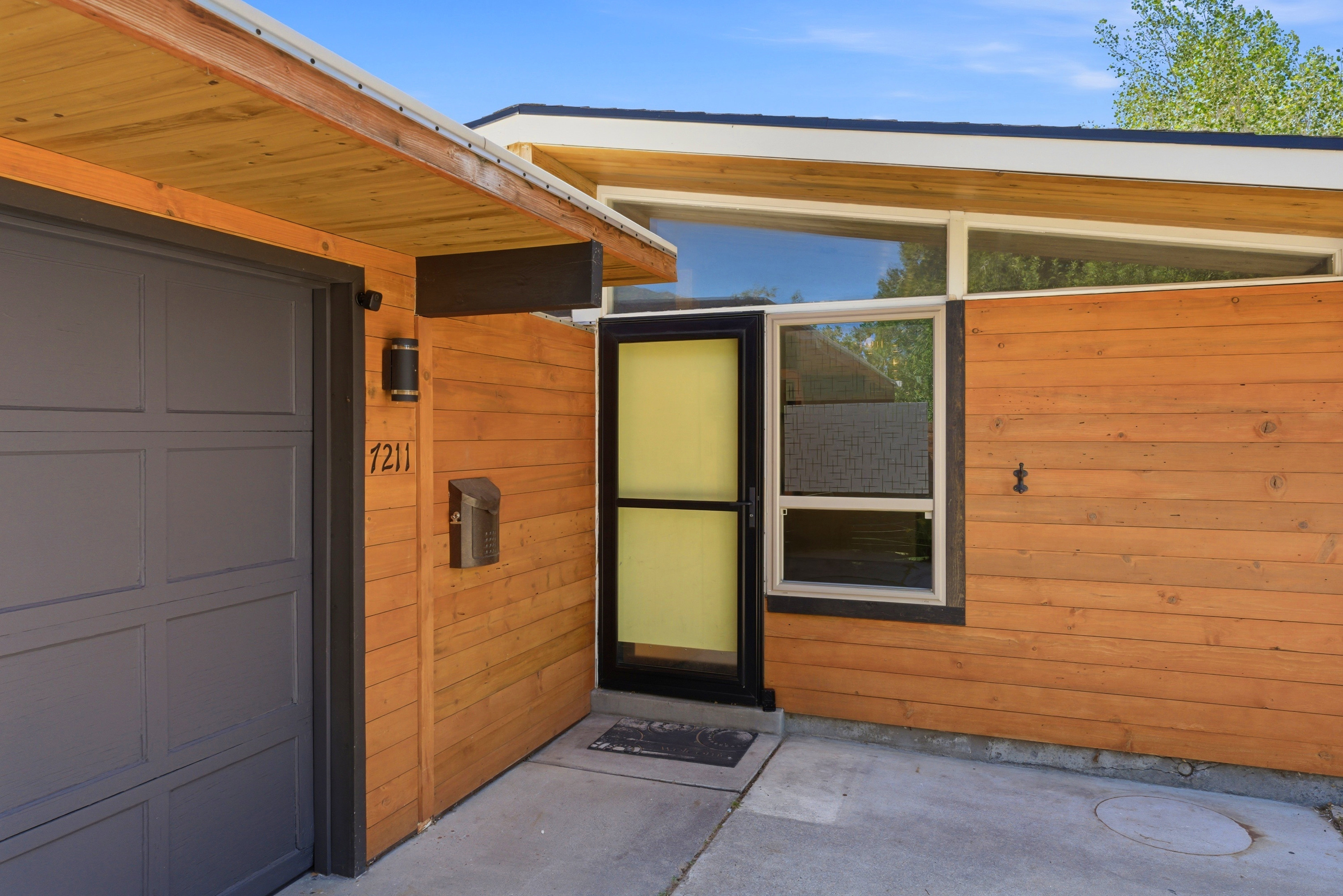 Modern architectural exterior featuring wood paneling, a gray paneled garage door, and a black front entry door