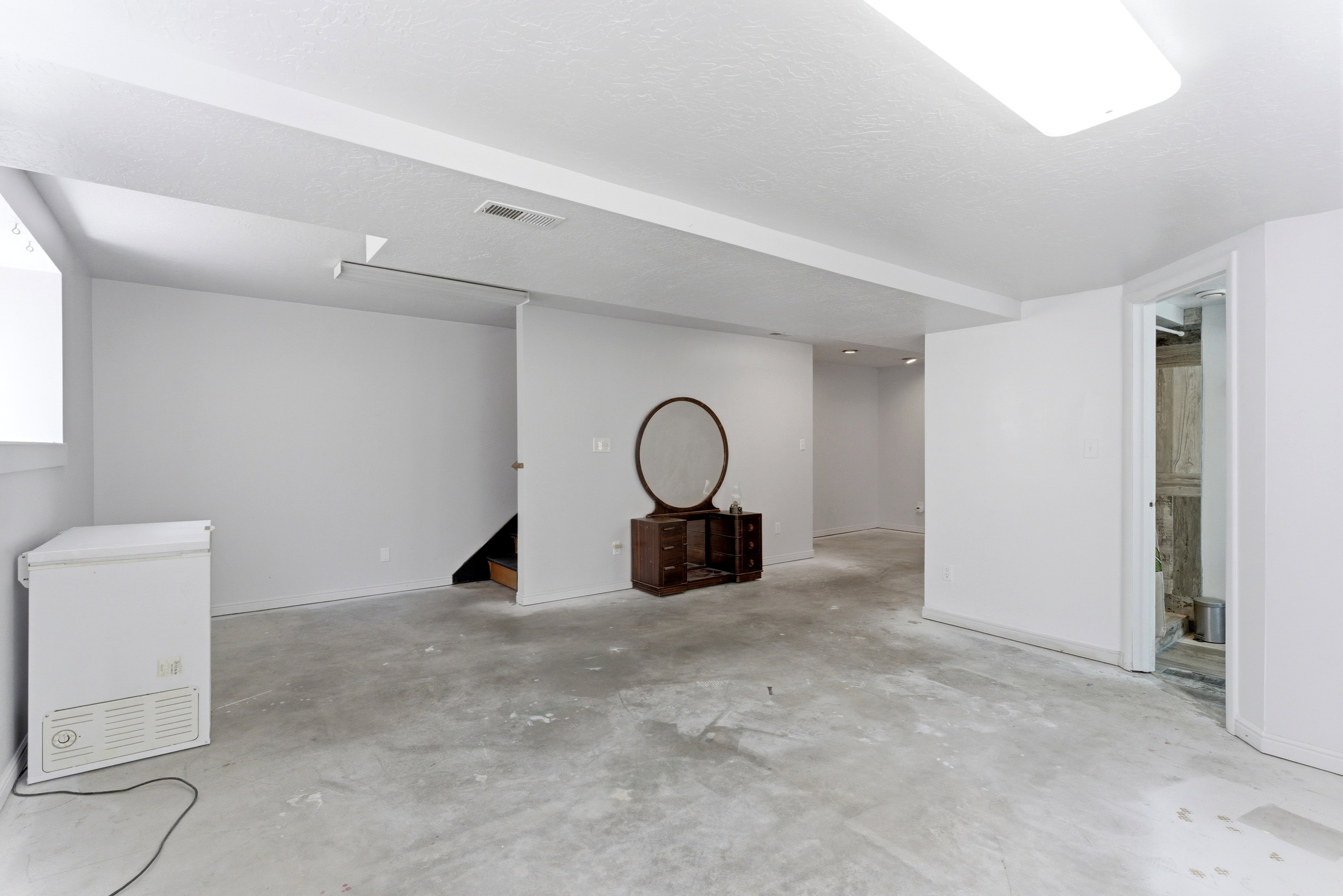 Spacious lower-level area with concrete flooring, white painted walls, and overhead fluorescent lighting