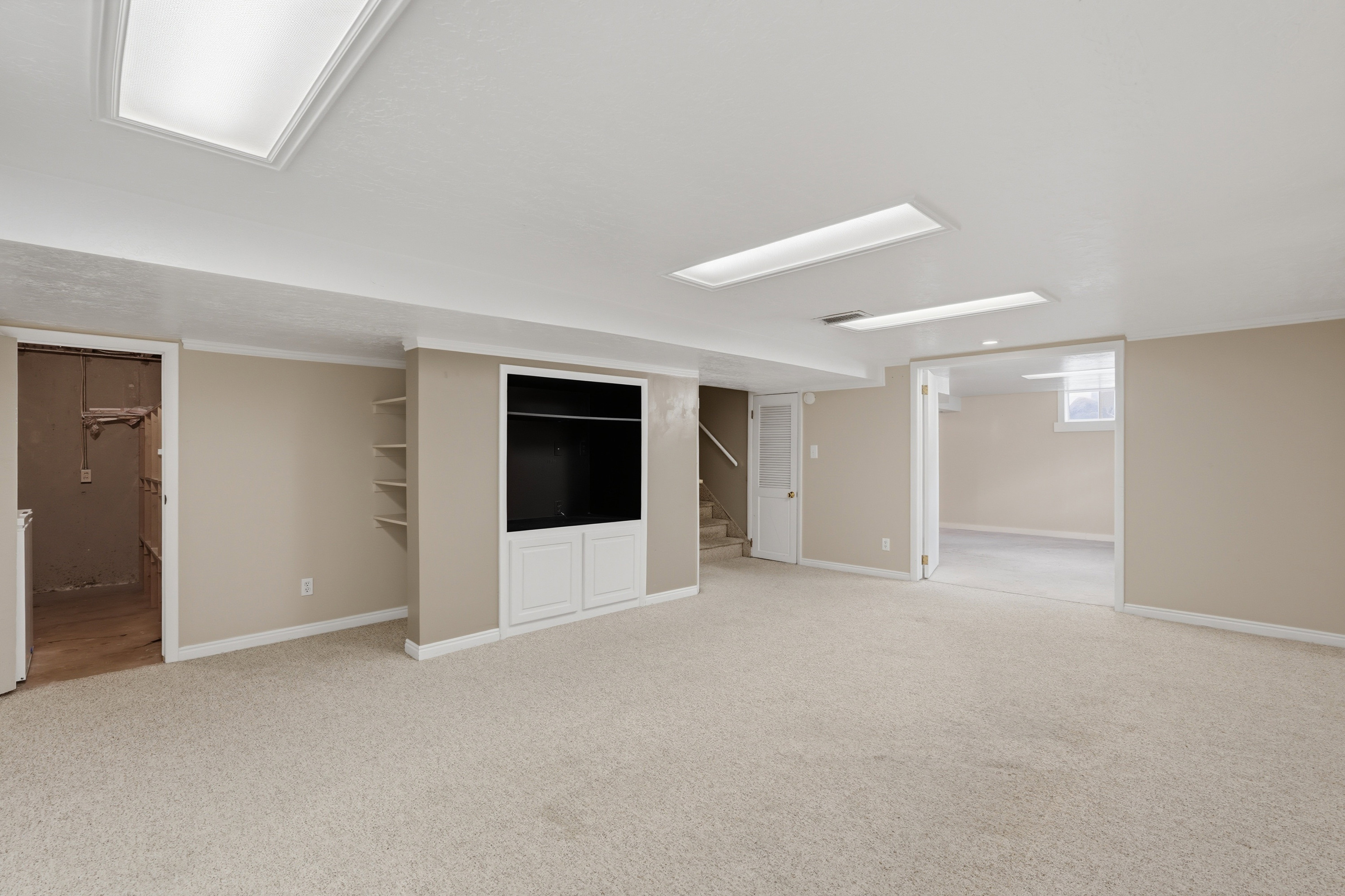 Expansive carpeted area featuring a built-in media cabinet with lower storage, recessed lighting, and wall shelving