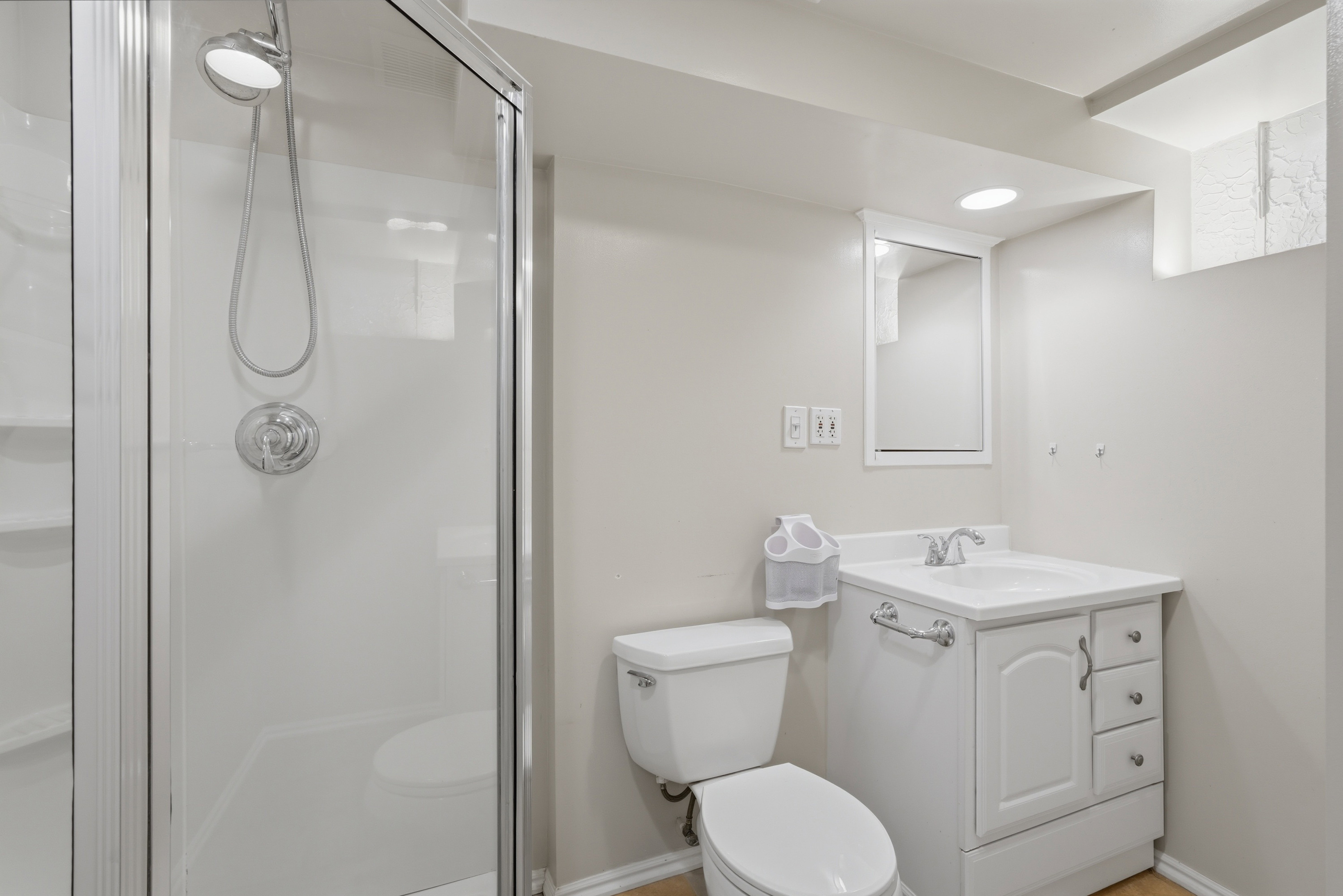 Three-piece bathroom featuring a glass-enclosed shower with a handheld showerhead, a white vanity with integrated sink and storage, and an illuminated medicine cabinet