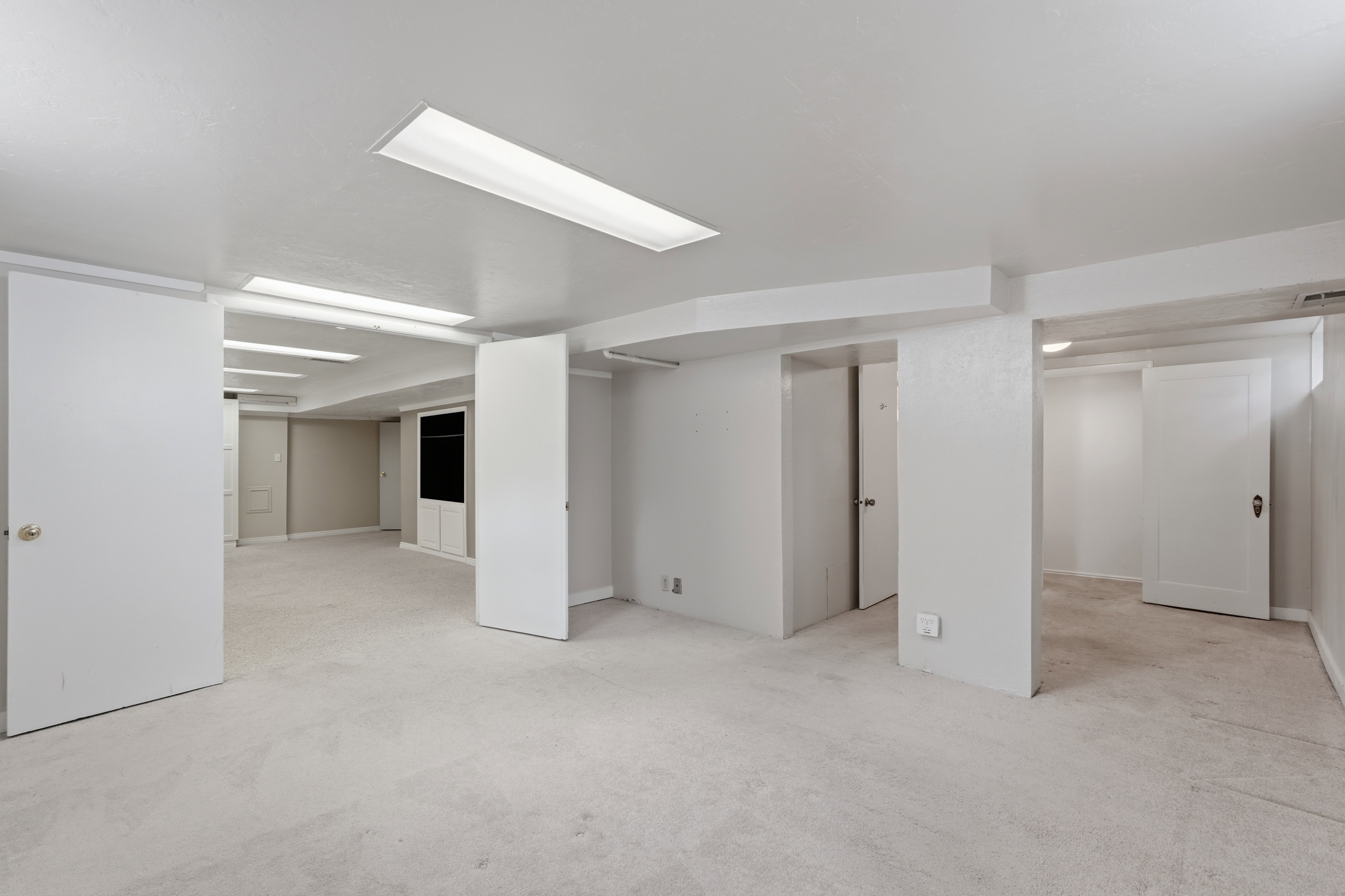 Spacious room featuring light-colored carpeting, white walls, and multiple recessed fluorescent lighting fixtures