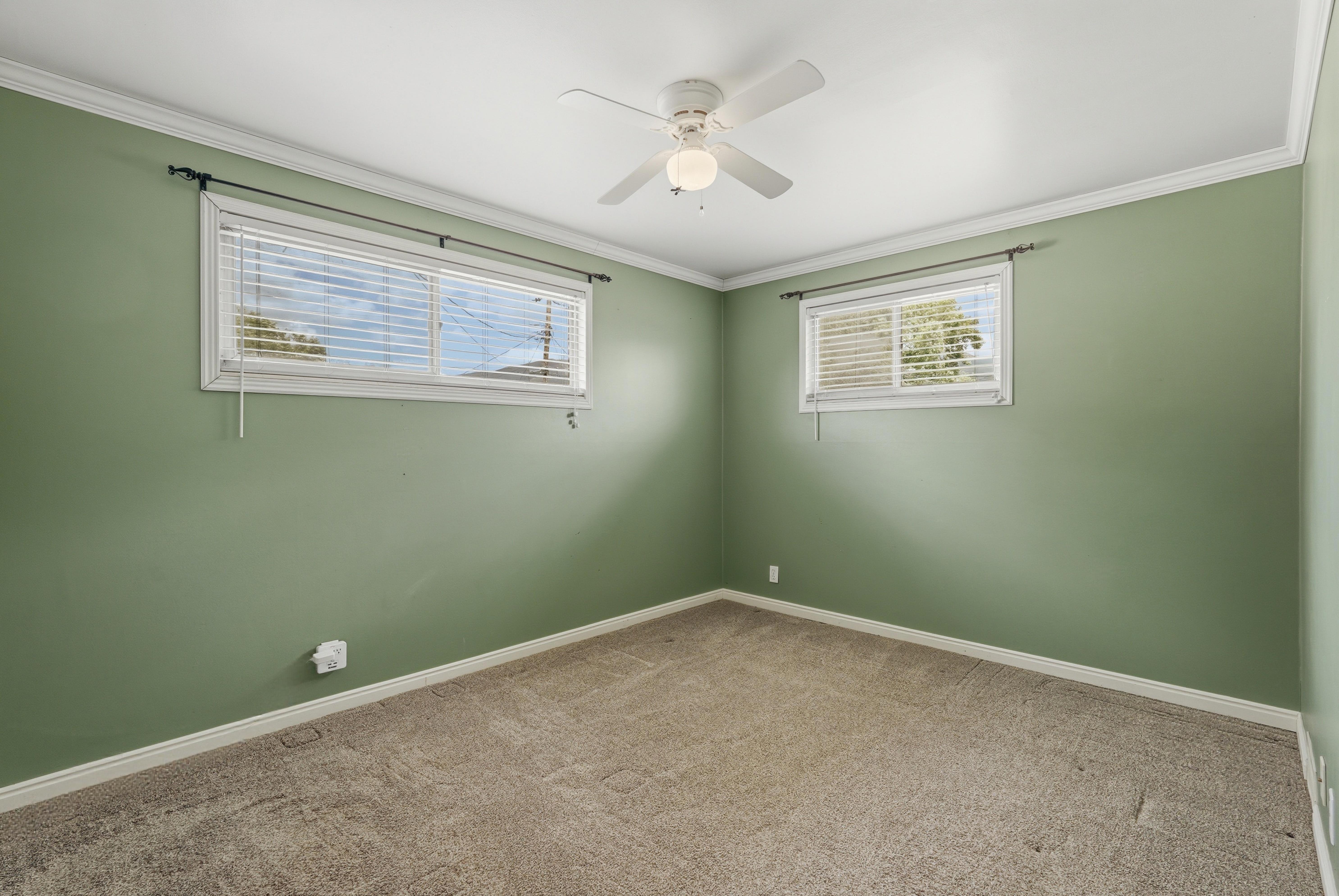 Room featuring two windows with horizontal blinds, a ceiling fan with integrated lighting, crown molding, and neutral-toned carpeting