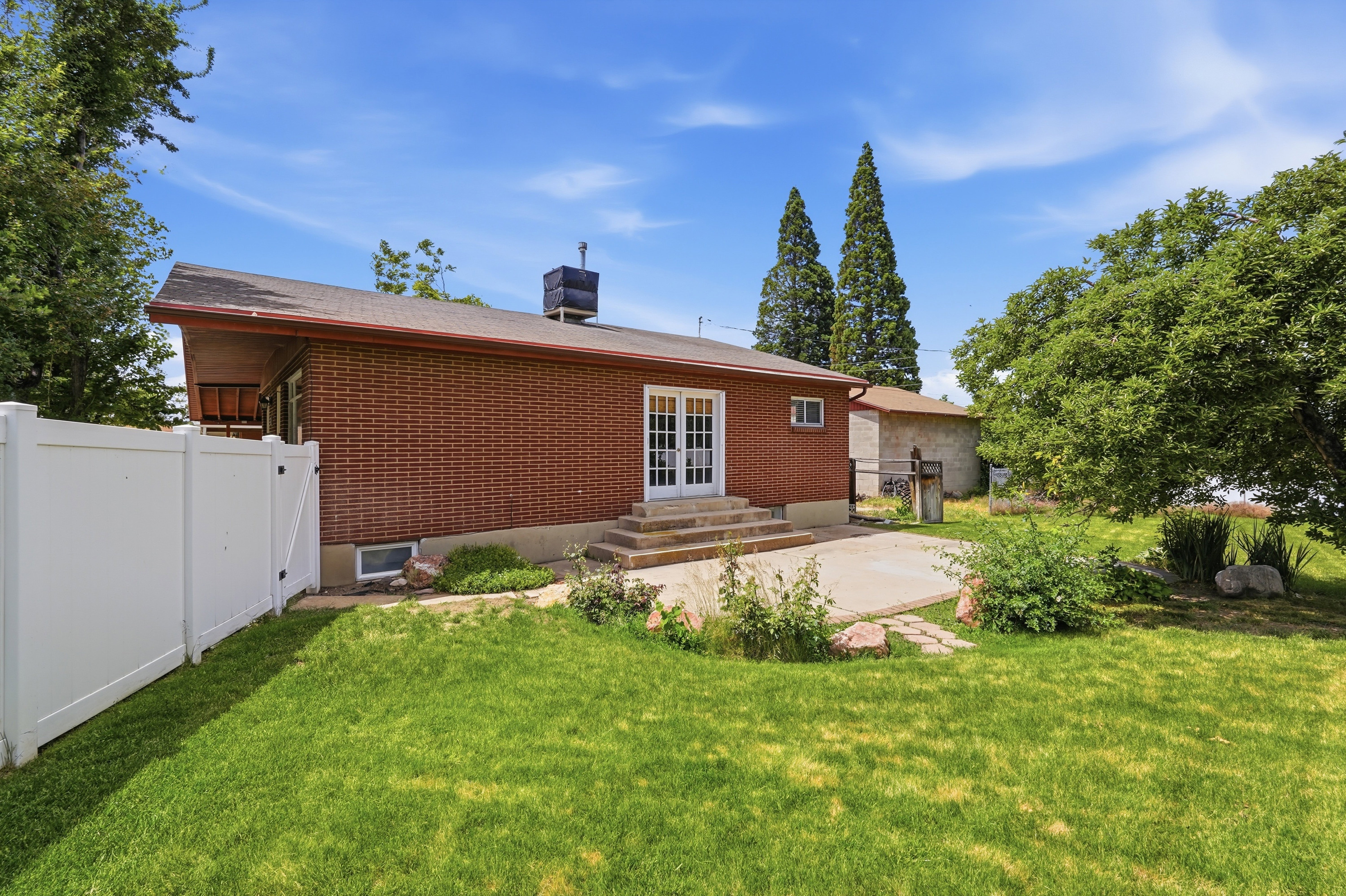 Expansive backyard featuring a manicured lawn, a concrete patio area, and mature trees