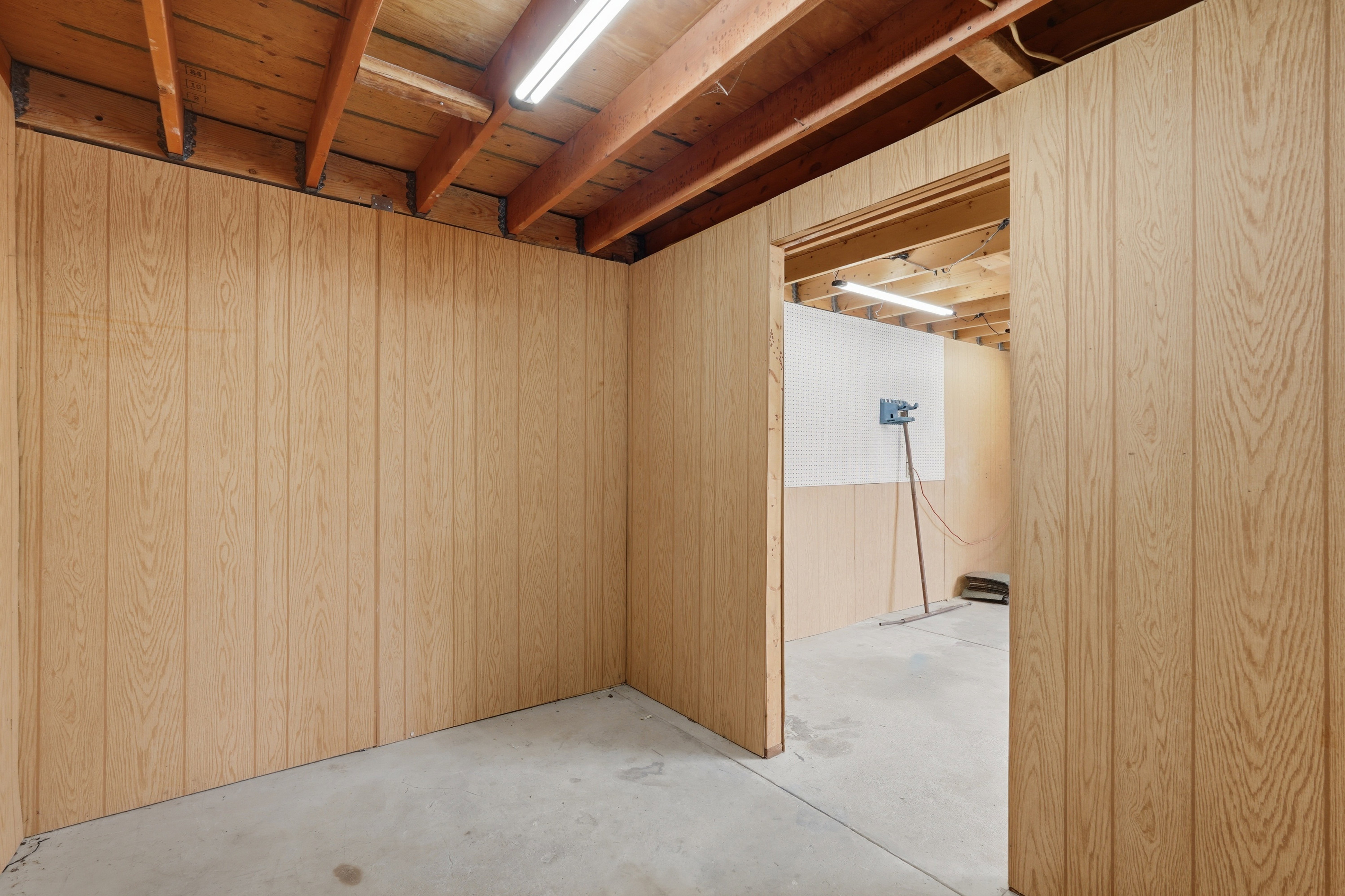 Wood-paneled room featuring exposed wood ceiling joists, concrete flooring, and fluorescent lighting