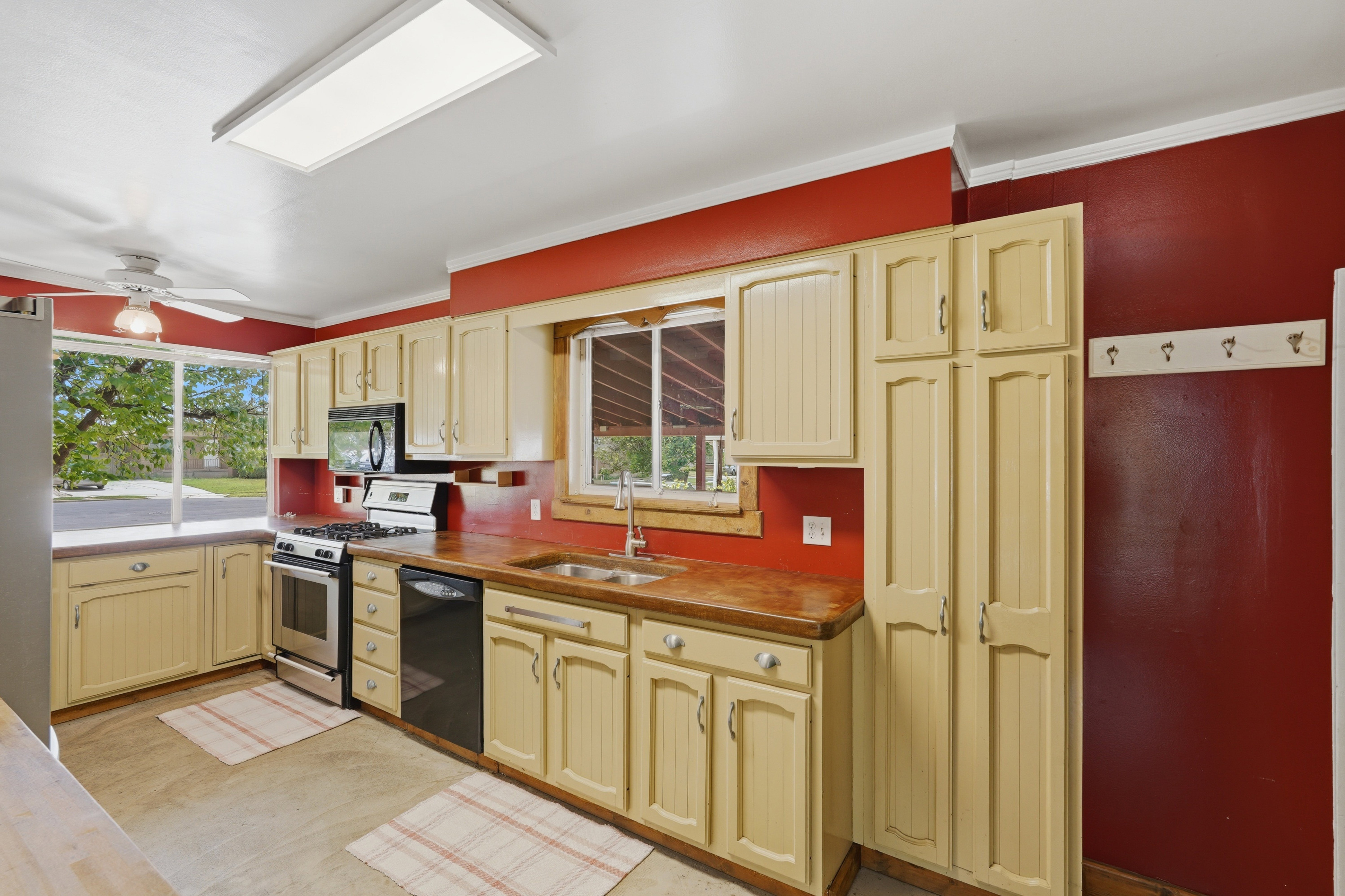 Kitchen featuring cream-colored cabinetry, stainless steel range, built-in microwave, dark-finish dishwasher, and a large window above a double-basin sink