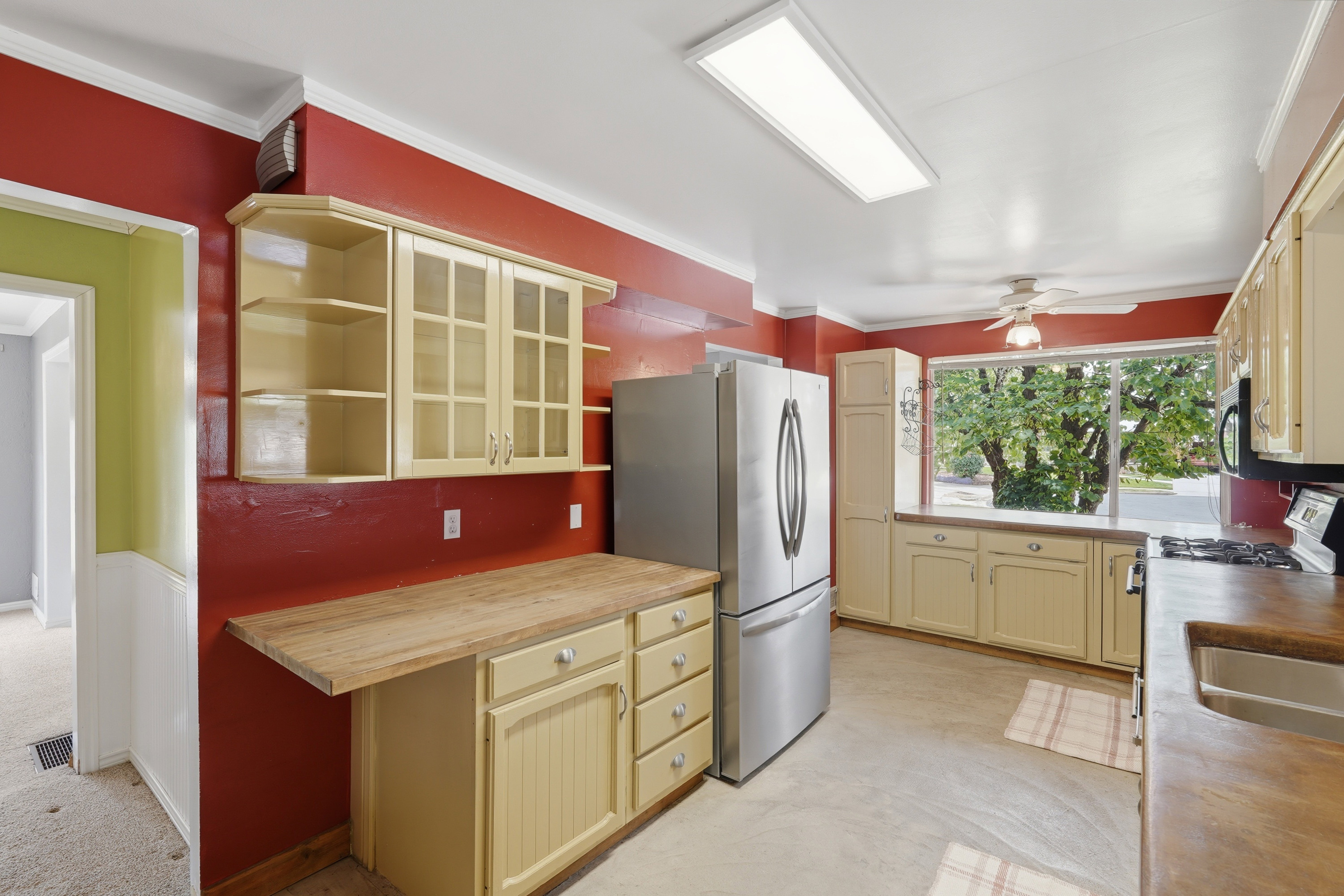 Kitchen featuring a large window, light-colored cabinetry with glass inserts, wood-finish countertops, and a stainless steel refrigerator