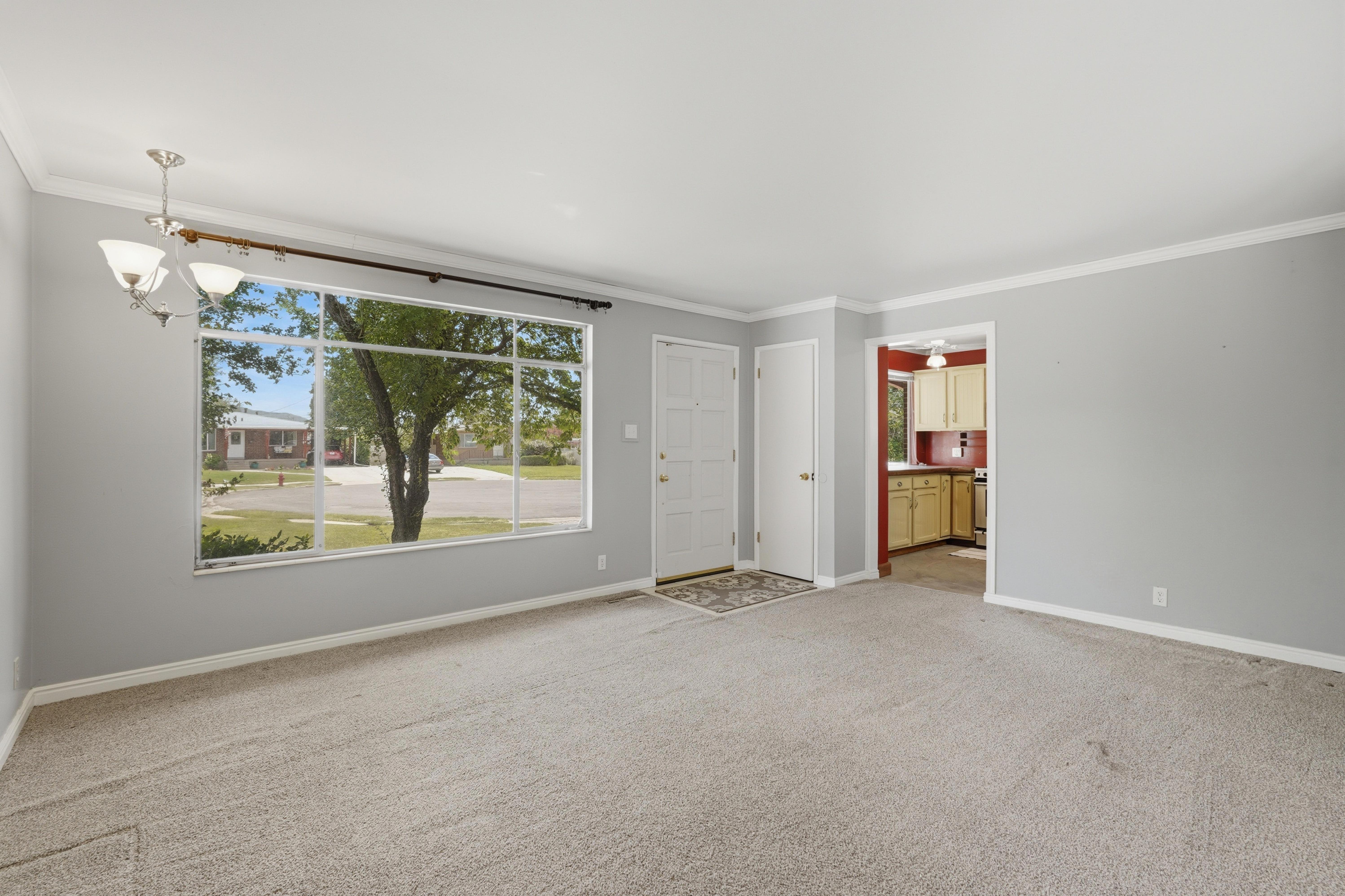 Living area featuring a large picture window, a flush-mount chandelier, light-toned carpeting, and a white entry door