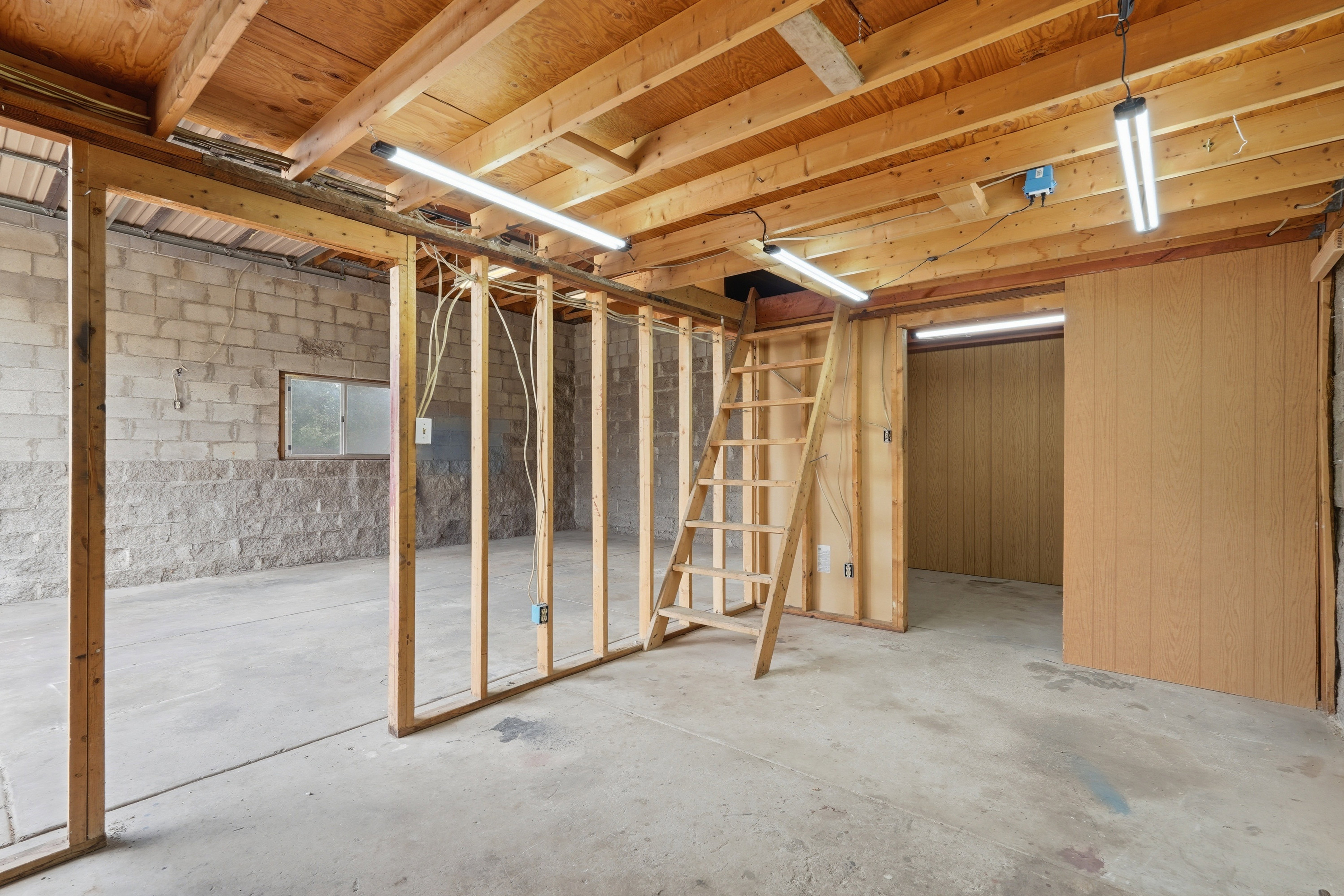 Unfinished lower level featuring exposed wood beam ceiling, concrete block walls, and a concrete floor