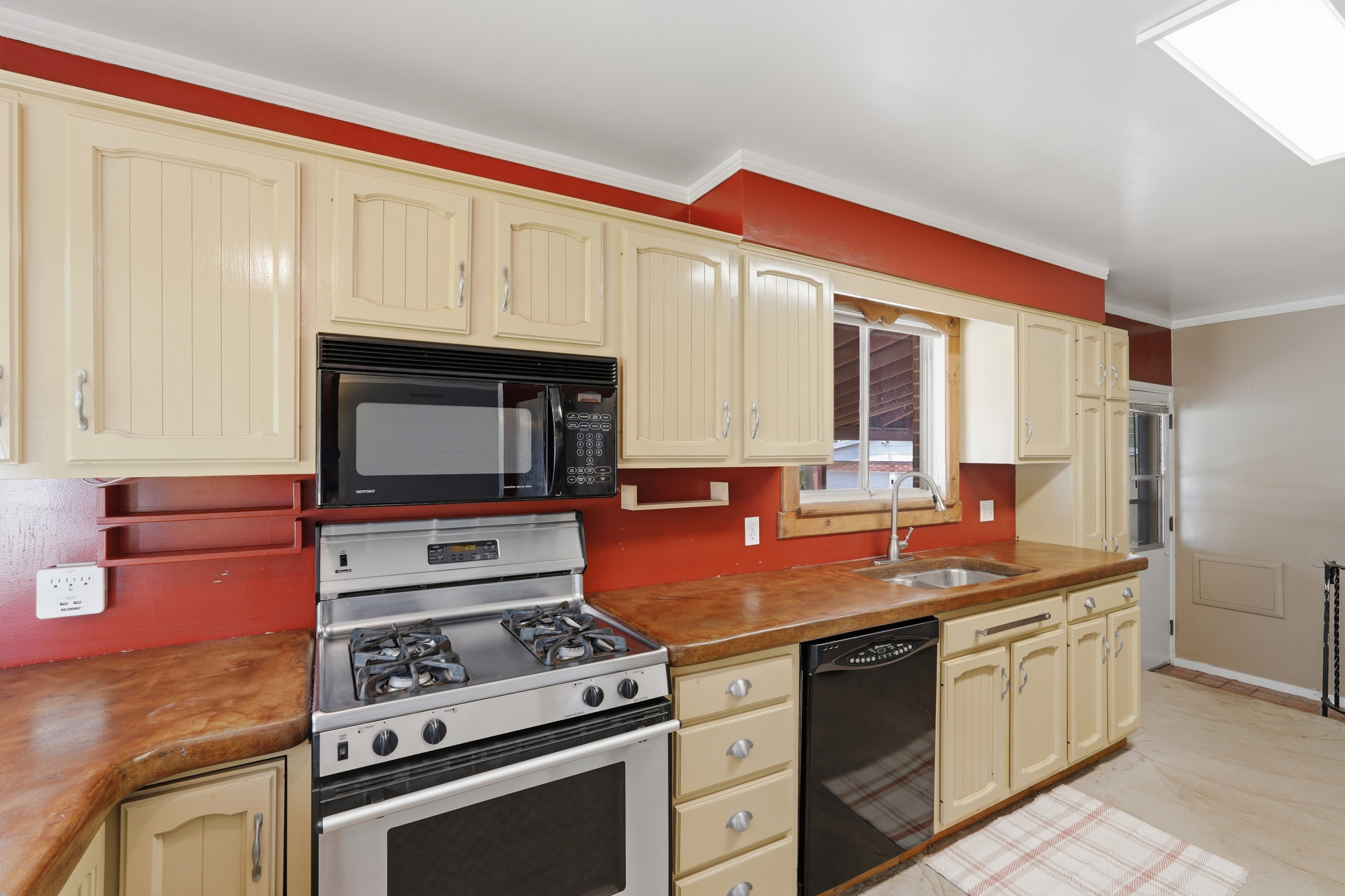 Kitchen featuring cream-painted cabinetry, a stainless steel gas range, an over-the-range microwave, and a black dishwasher