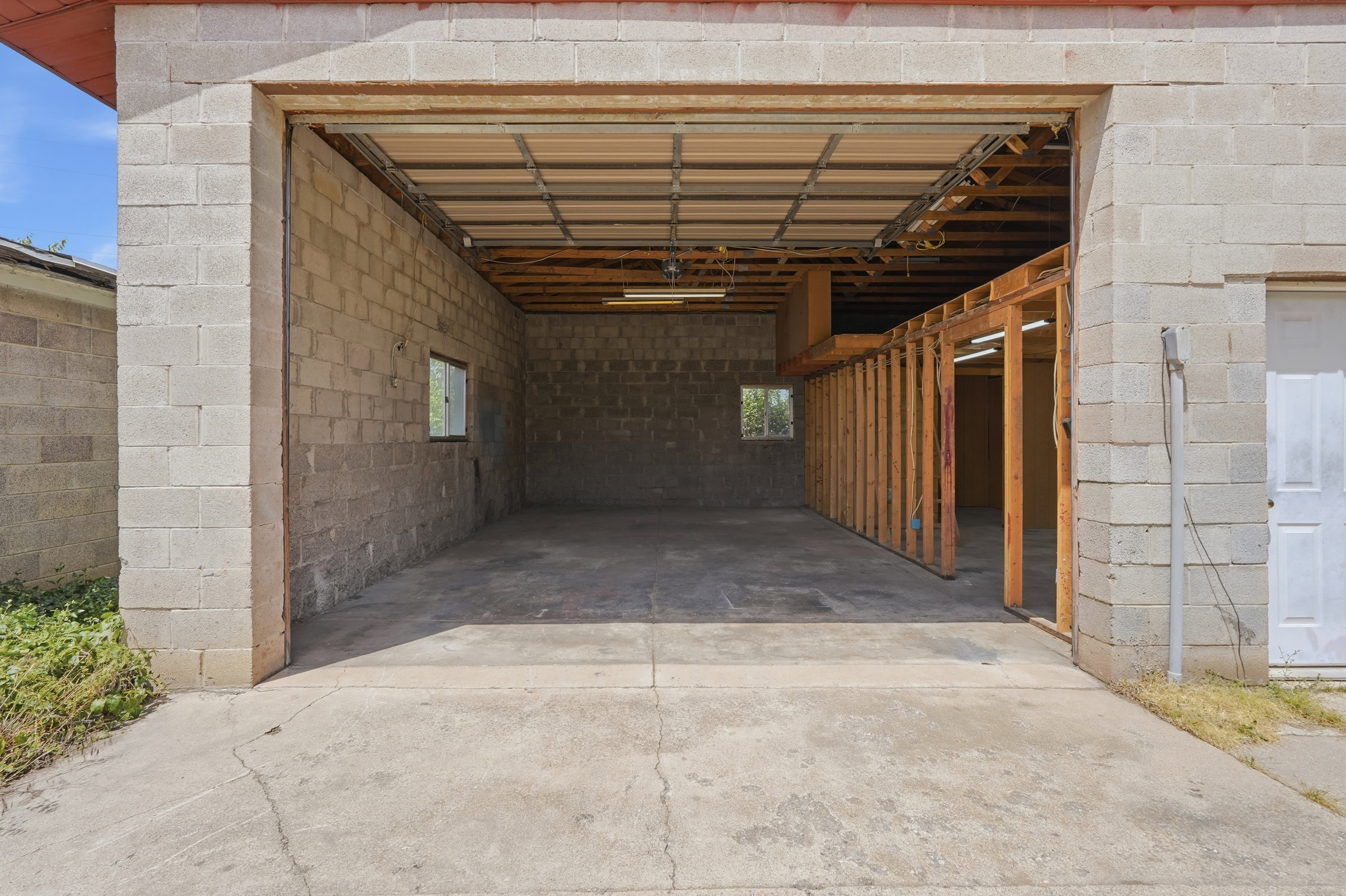 Spacious block construction garage featuring a concrete floor, exposed ceiling joists, and framed interior partitions