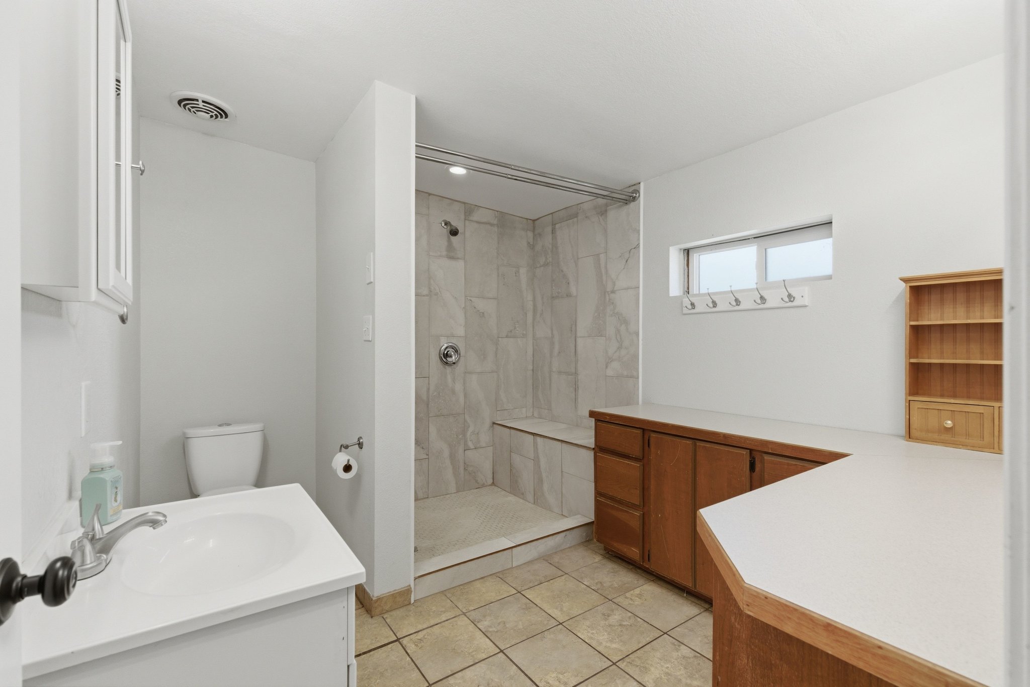 Bathroom featuring a tiled walk-in shower with a built-in bench, a single vanity with a white countertop, and extensive counter space with wood-finish cabinetry