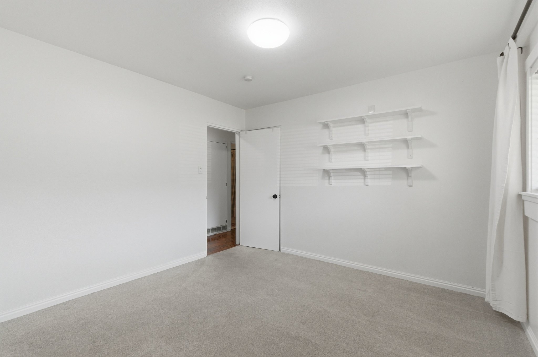 Bright room featuring light gray carpeting, white walls, and a window with white trim