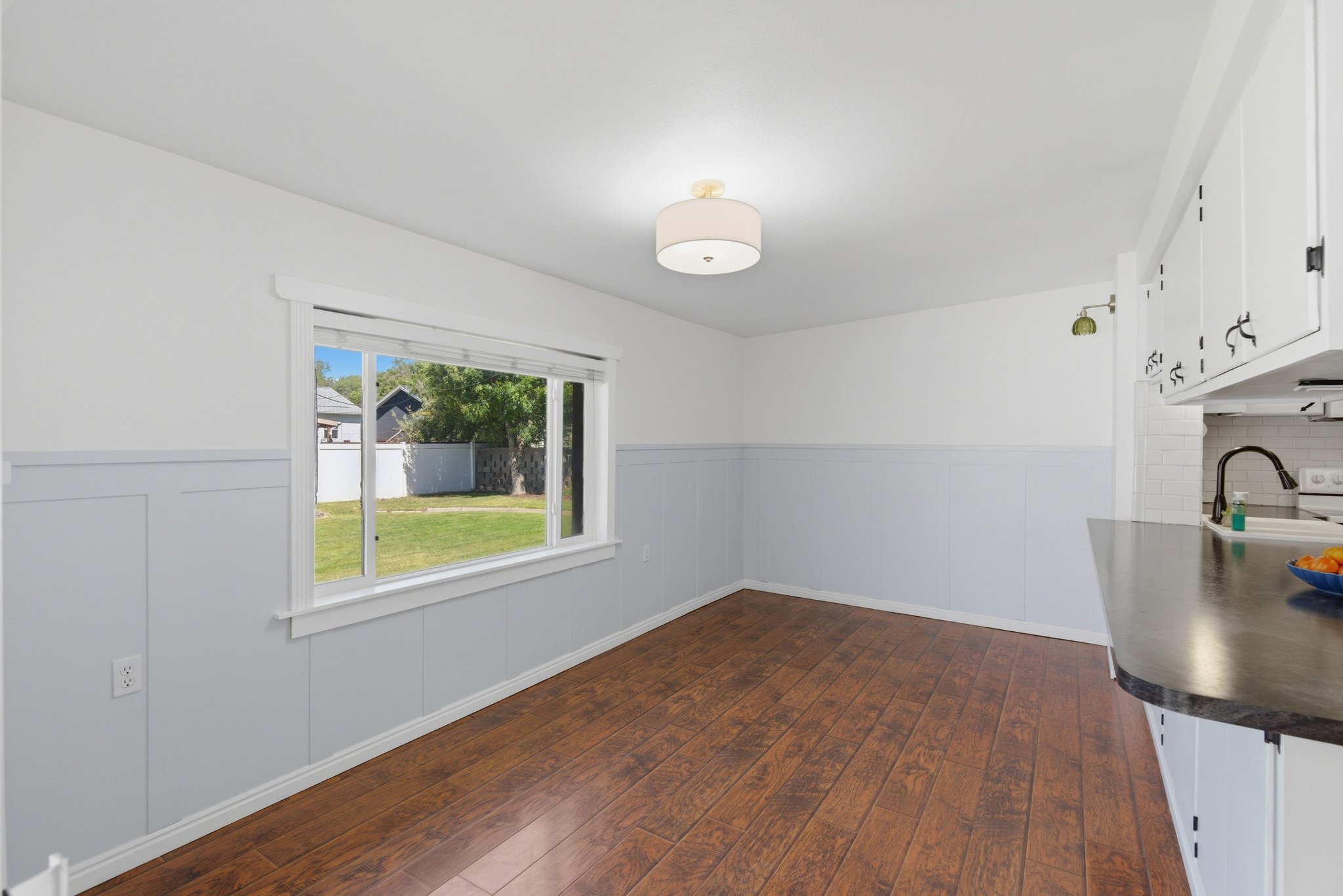 Dining area featuring wood-finish flooring, a large window, a semi-flush mount ceiling light, and paneling on the lower walls