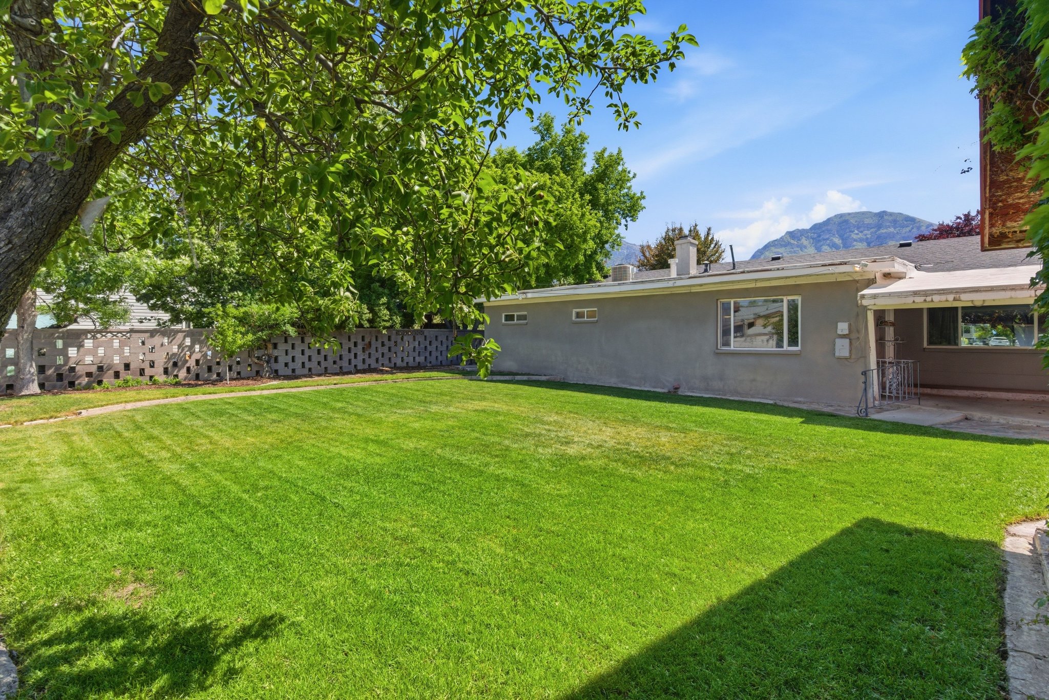 Expansive lawn featuring a mature shade tree and decorative concrete block fencing