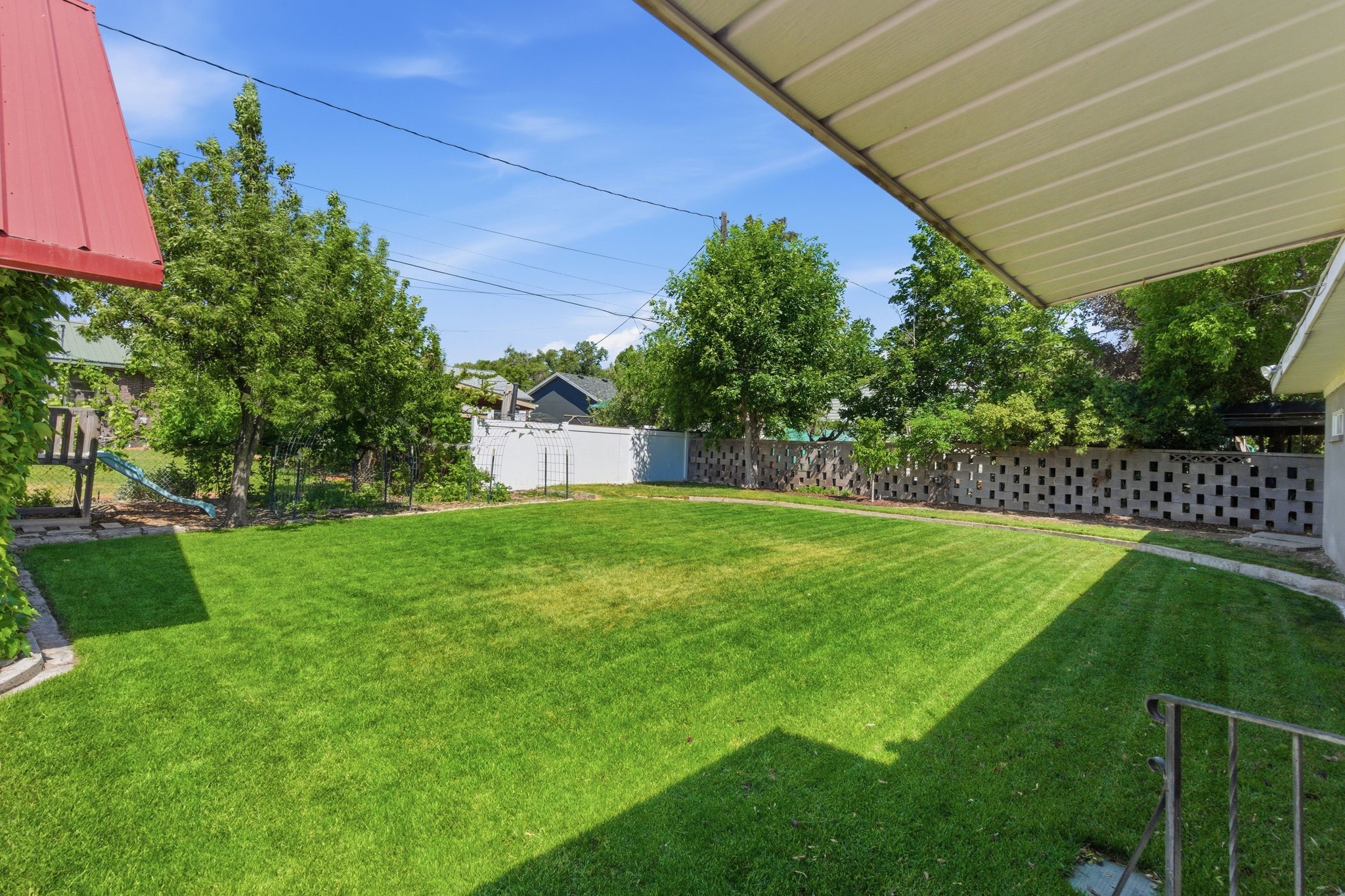 Spacious rear yard featuring an expansive lawn, mature perimeter trees, and a decorative block privacy fence