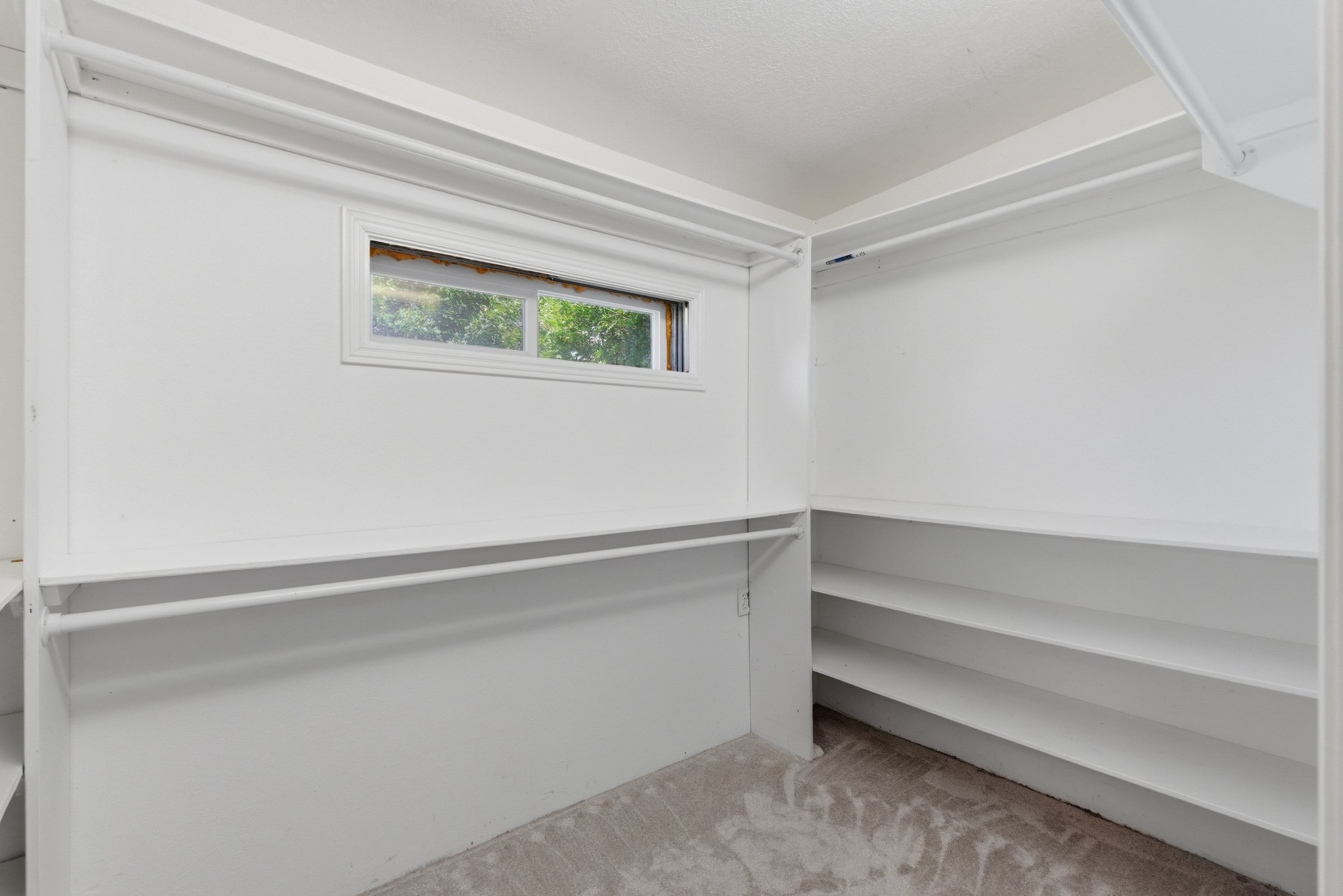 Walk-in closet with integrated shelving, multiple hanging rods, and a window