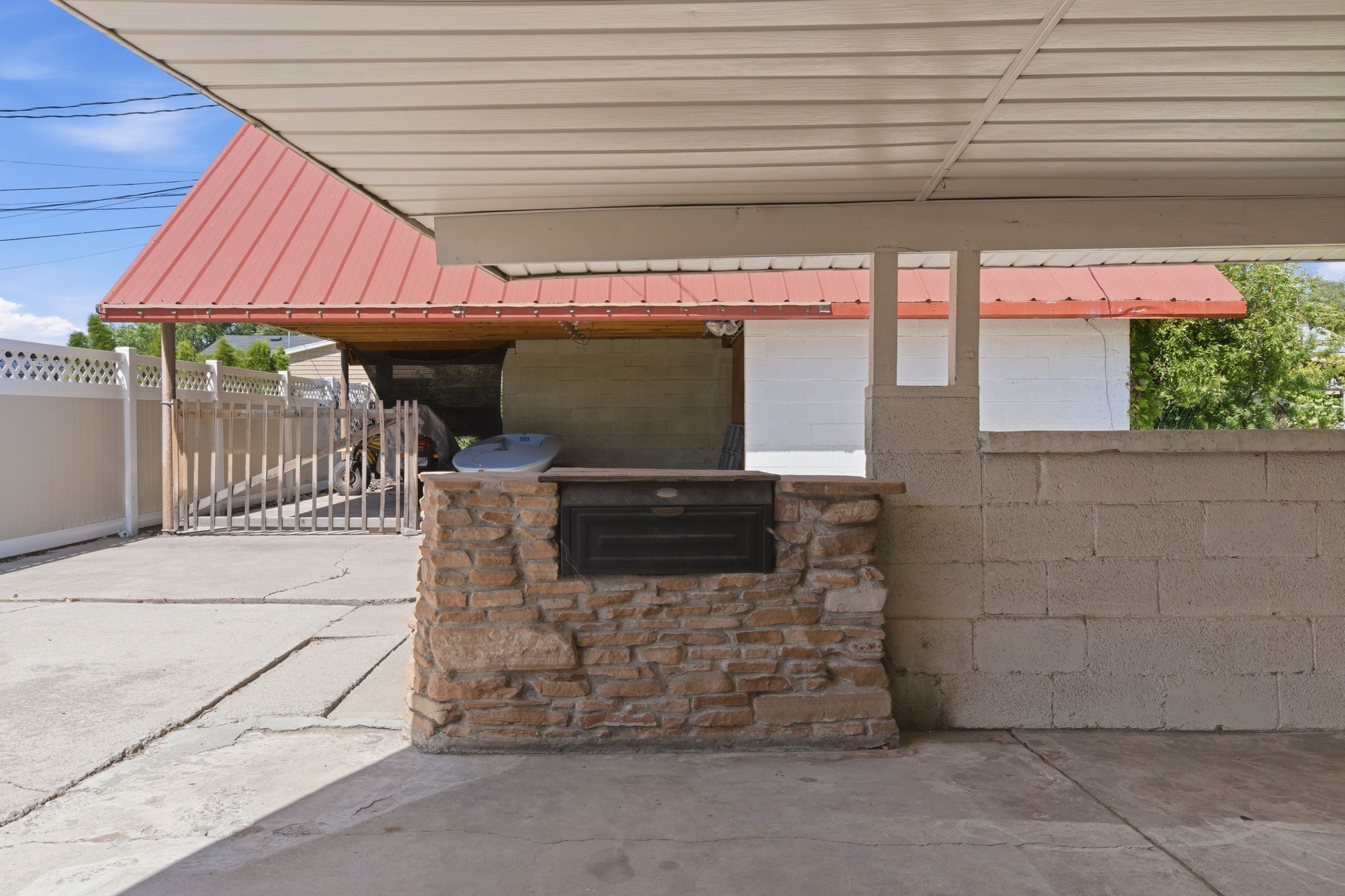 Covered patio area featuring a built-in stone-clad grill station, concrete block half-wall, and a concrete pad