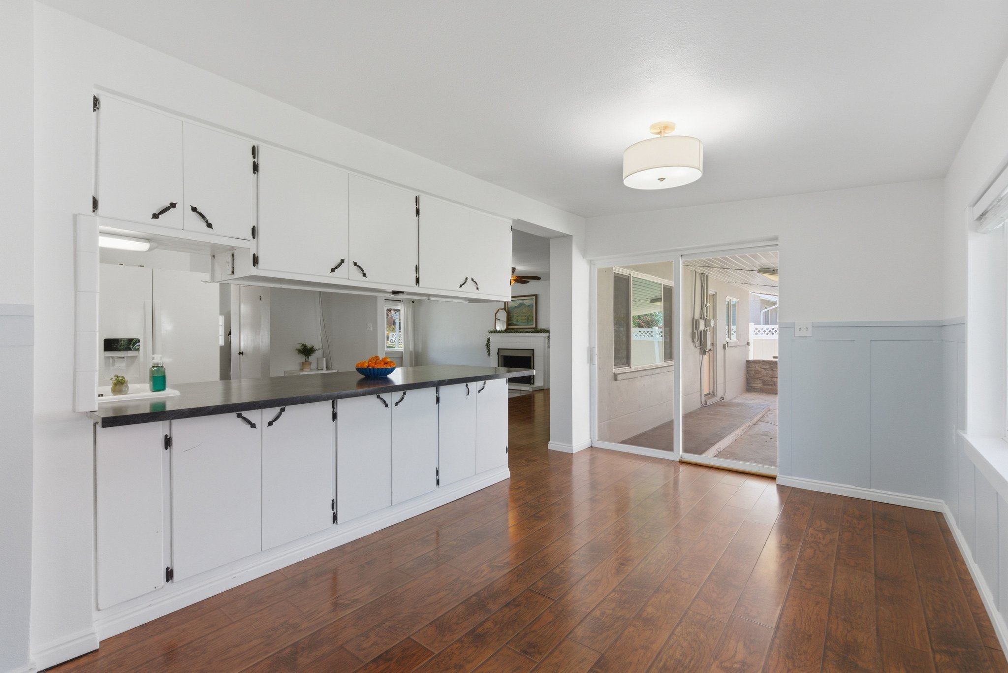 Spacious kitchen and dining area featuring extensive white cabinetry, dark countertops, wood-finish flooring, a contemporary ceiling fixture, and sliding glass door access to an outdoor patio
