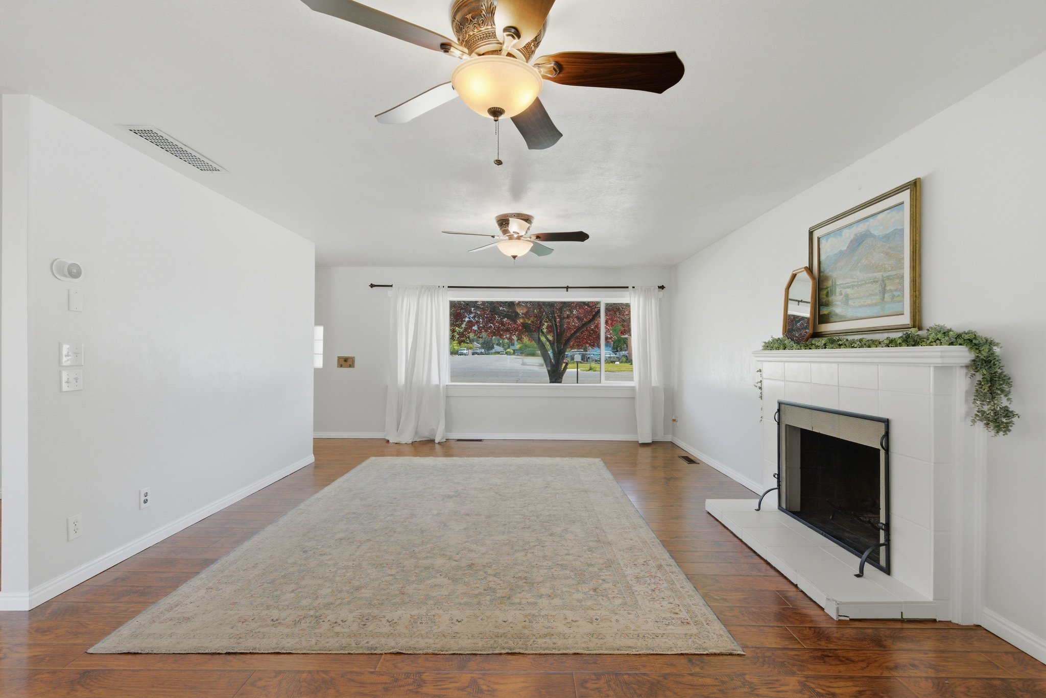 Living area featuring wood-finish flooring, a white tiled fireplace, and a large window