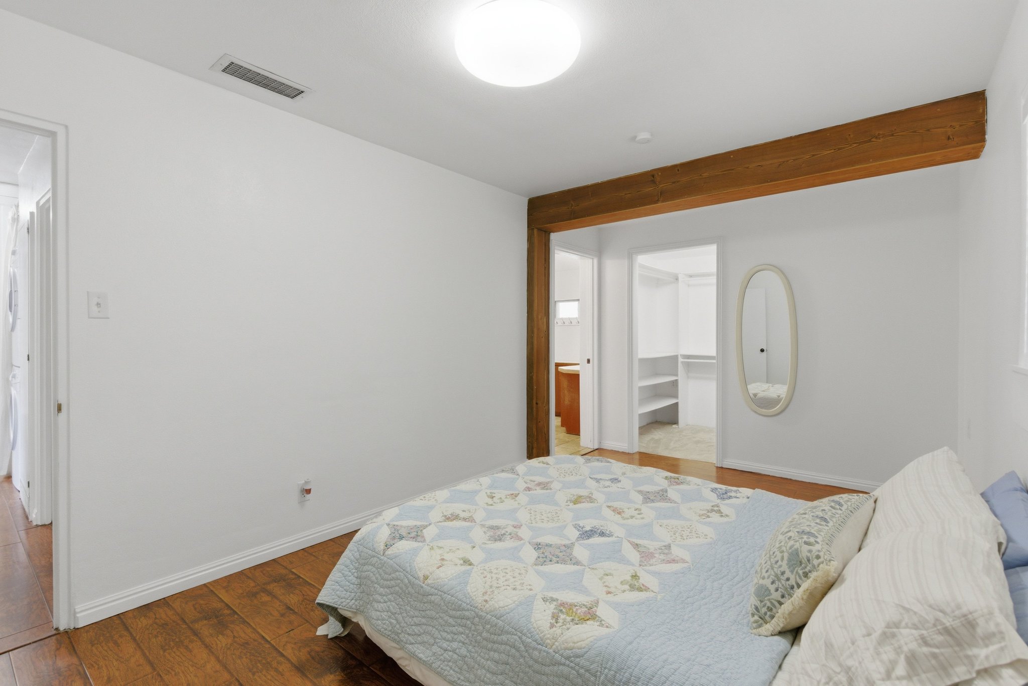 Bedroom featuring wood-finish flooring, a prominent exposed wood beam, and a ceiling-mounted flush light fixture