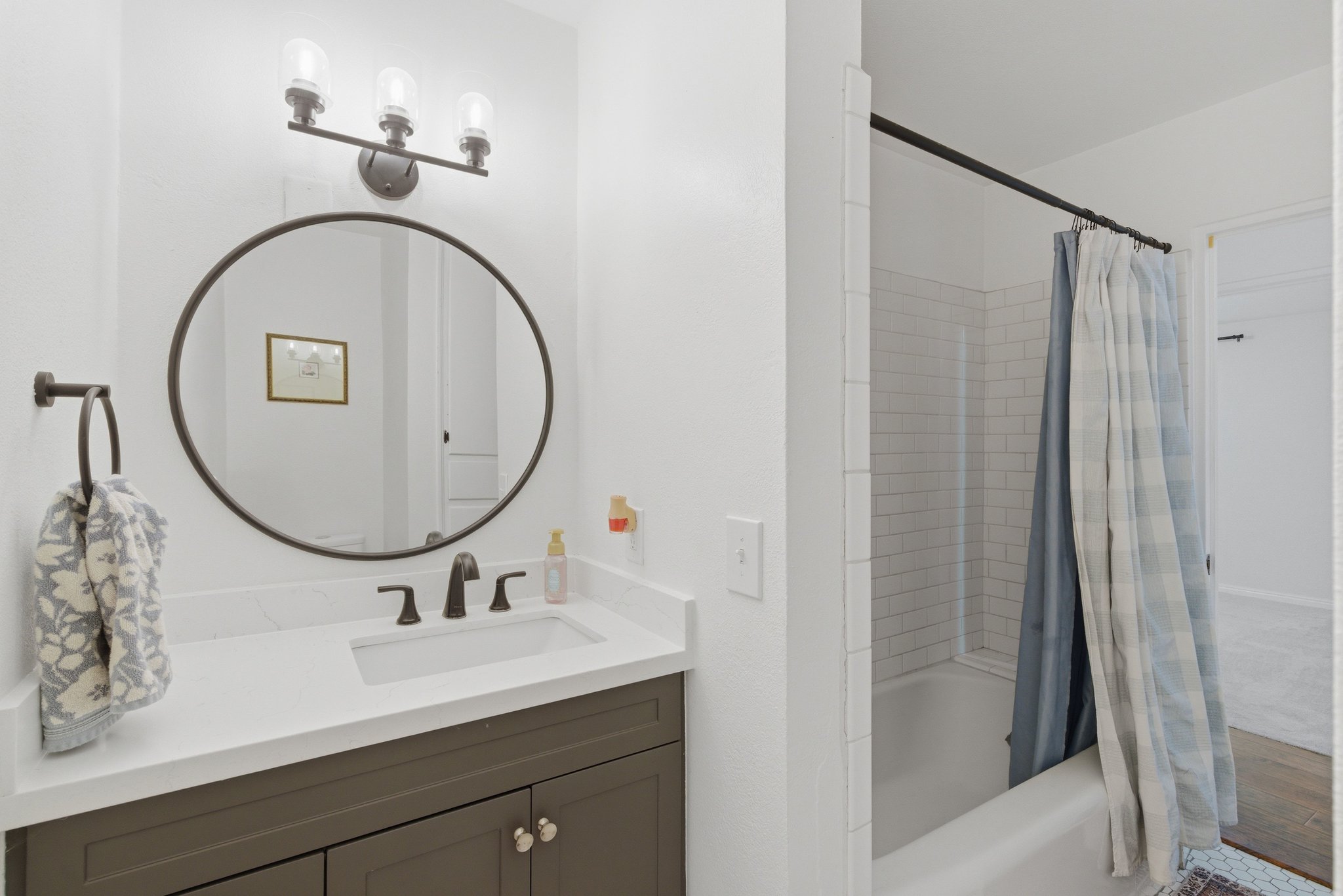 Bathroom vanity with a white countertop and dark gray cabinetry, featuring an undermount sink and a circular framed mirror