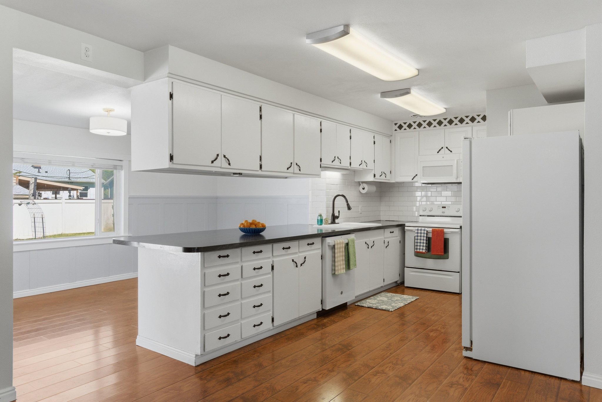 Kitchen featuring white cabinetry, dark countertops, a subway tile backsplash, and wood-finish flooring