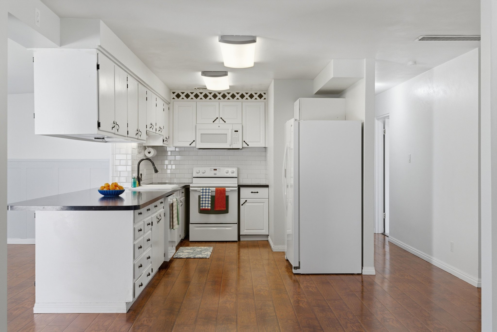 Kitchen featuring wood-finish flooring, white cabinetry, a black countertop, white subway tile backsplash, and overhead lighting