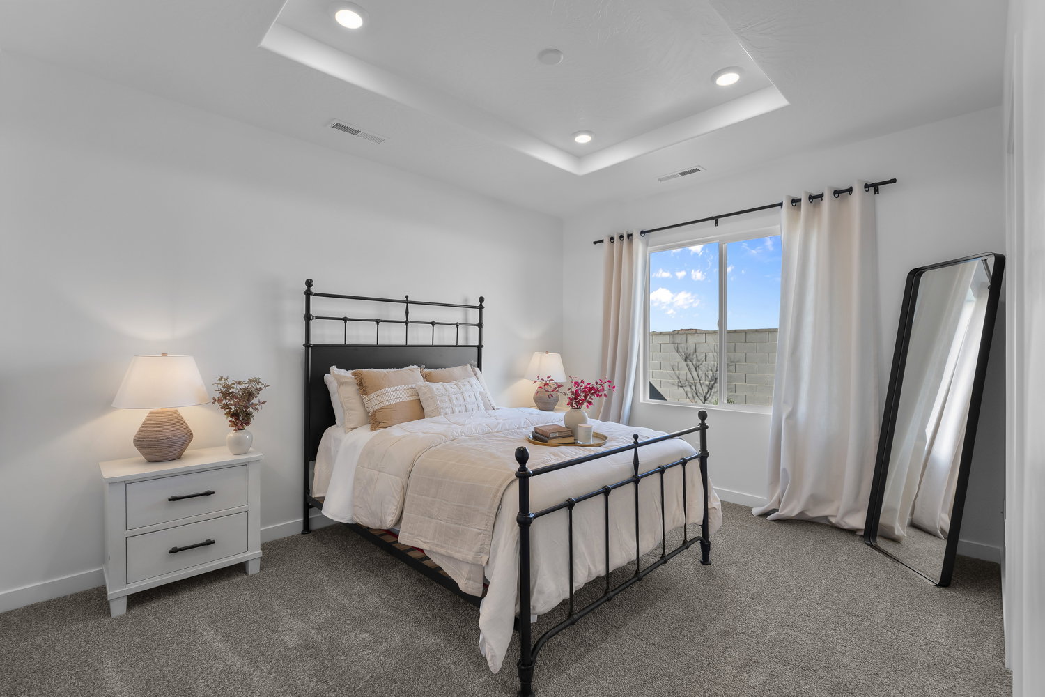 Recessed lighting highlights the tray ceiling in this room featuring a double window, wall-to-wall carpeting, and bright white walls