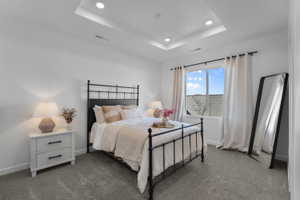Recessed lighting highlights the tray ceiling in this room featuring a double window, wall-to-wall carpeting, and bright white walls
