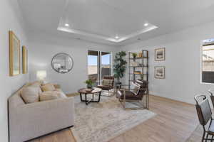Light-filled living space featuring wood-finish flooring, a tray ceiling with recessed lighting, and a sliding glass door for outdoor access