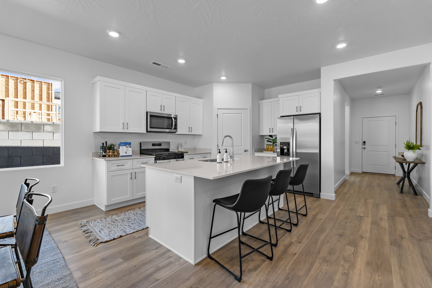 Modern kitchen featuring white shaker cabinetry, stainless steel appliances, a large center island with seating, recessed lighting, and wood-finish flooring