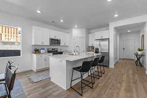 Modern kitchen featuring white shaker cabinetry, stainless steel appliances, a large center island with seating, recessed lighting, and wood-finish flooring