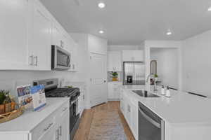 Modern kitchen featuring white shaker cabinetry, stainless steel appliances, quartz countertops, and wood-finish flooring