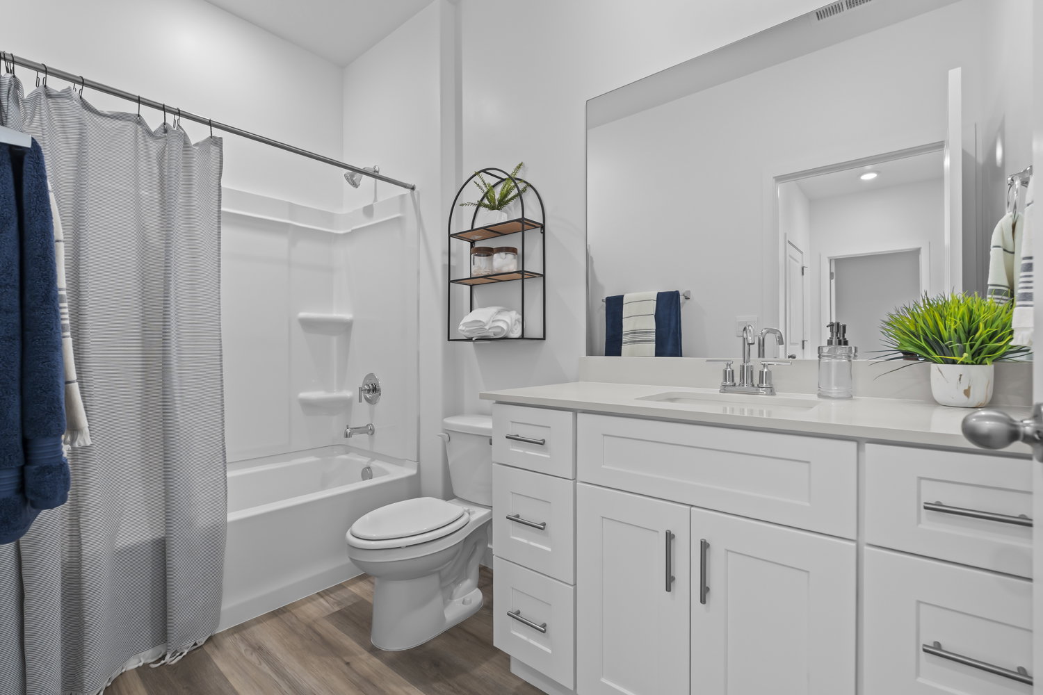 Bathroom featuring a white vanity with extensive storage, a large mirror, a bath-shower combination with a single-handle faucet, and wood-finish flooring