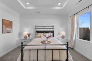 Bedroom featuring a tray ceiling with recessed lighting, a large window, white walls, and gray carpet