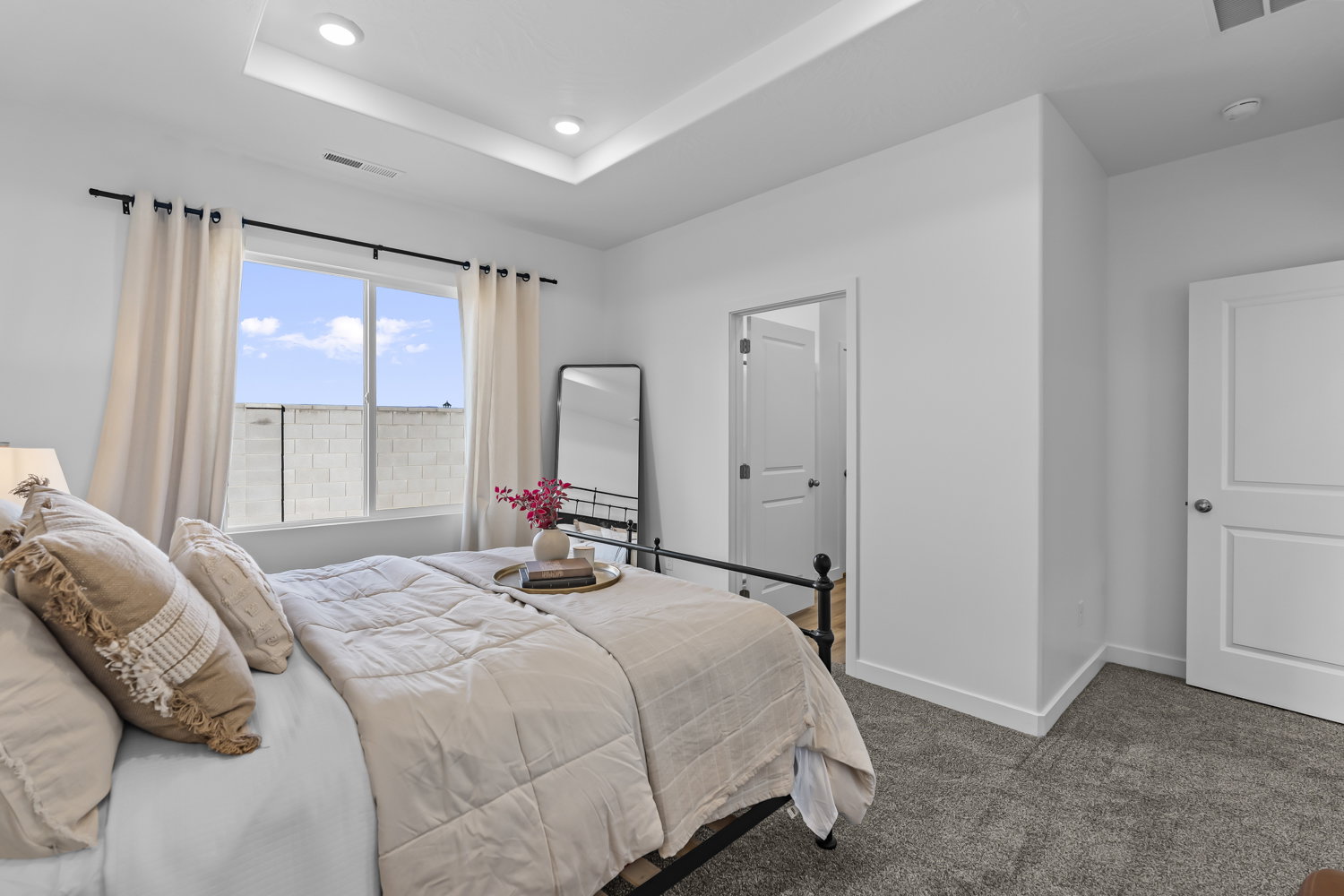 Spacious bedroom featuring a tray ceiling with recessed lighting, large windows, plush carpeting, and crisp white walls