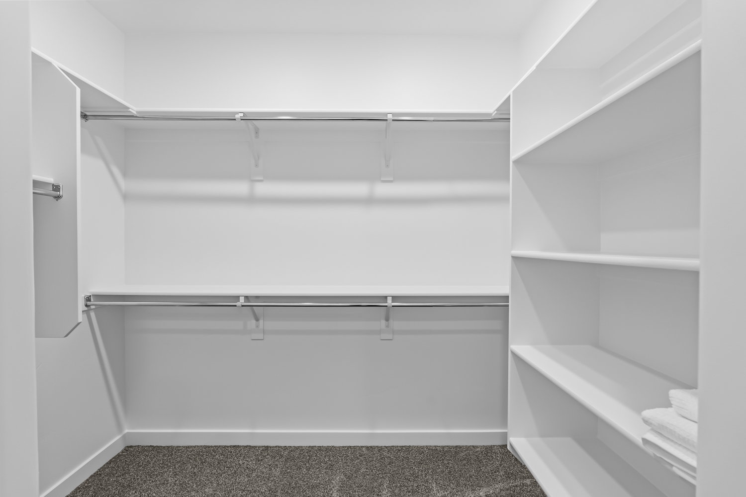 Walk-in closet featuring white wall shelving, multiple chrome hanging rods, and dark gray carpet flooring