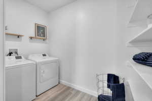 Dedicated laundry area featuring a washer and dryer, wood-finish flooring, white walls, two wall-mounted wood shelves, and built-in white shelving