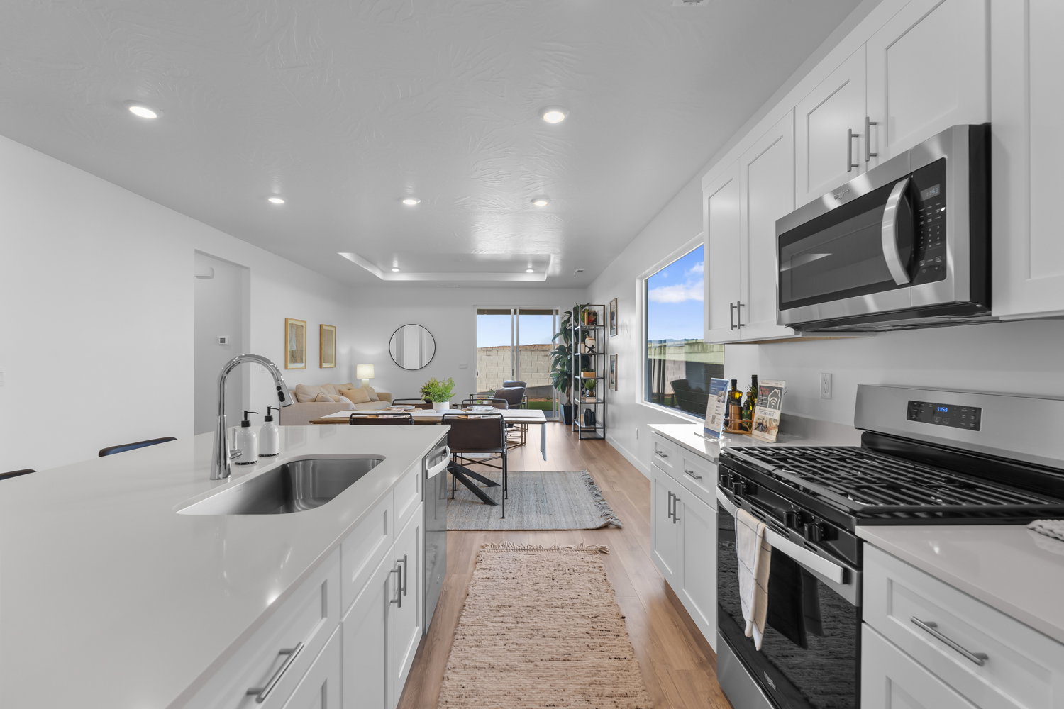 Modern kitchen featuring white cabinetry, stainless steel appliances, a large island with an undermount sink, and wood-finish flooring