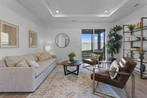 Spacious living area featuring a tray ceiling with recessed lighting, wood-finish flooring, and a large sliding glass door opening to a patio