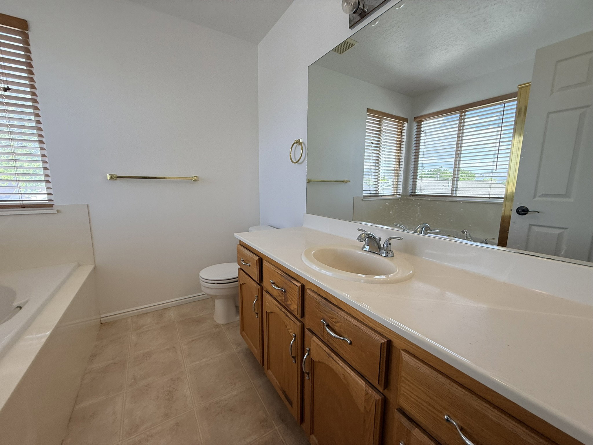 Bathroom featuring a built-in tub, wood-finish vanity with an integrated sink, and a large wall-mounted mirror