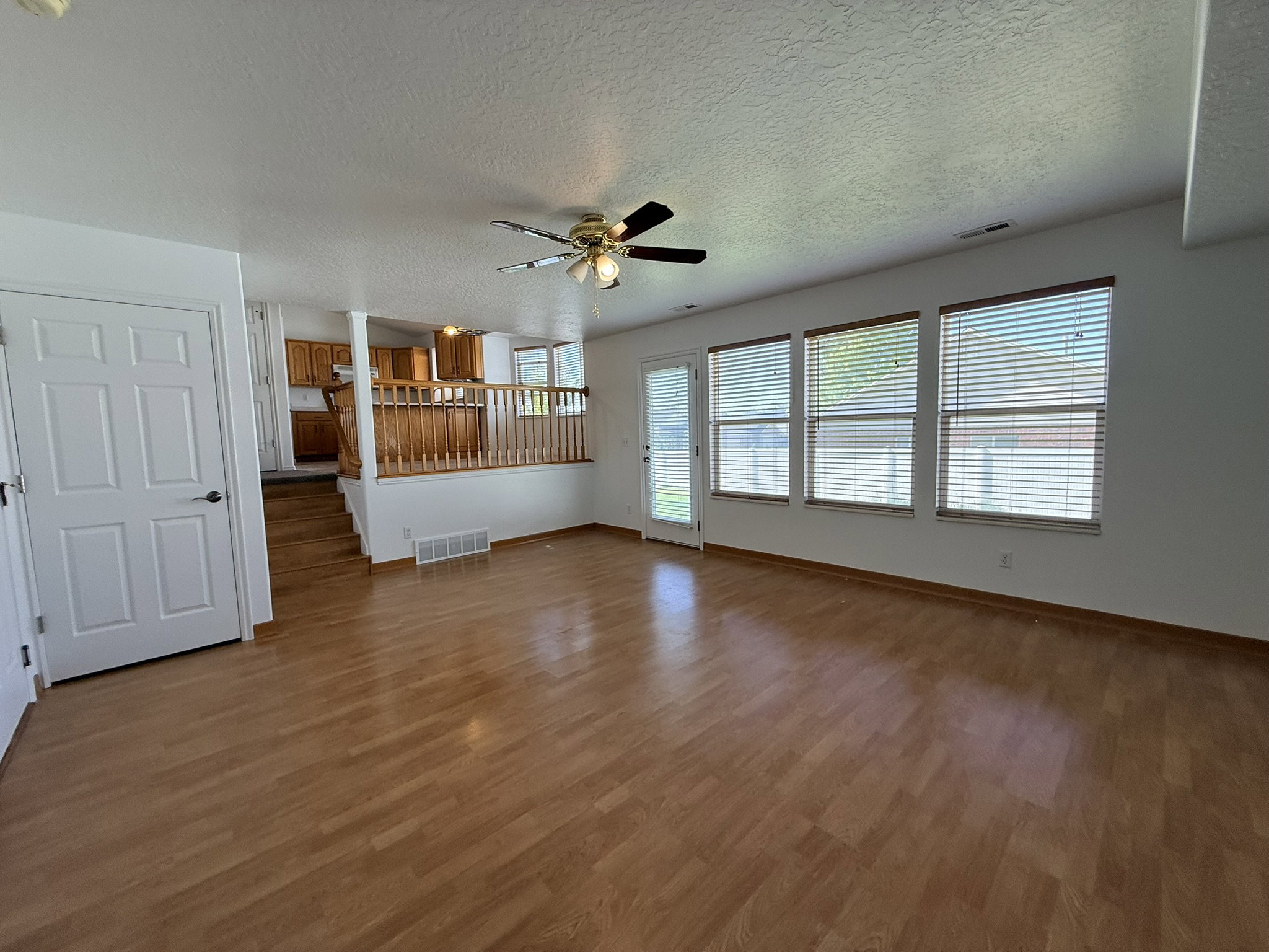 Spacious main living area featuring wood-finish flooring, a ceiling fan, and multiple windows with blinds