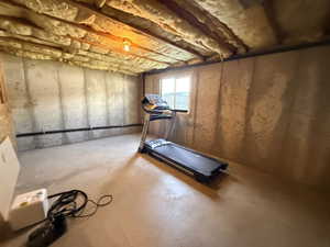 Daylight basement space featuring exposed wood joists with insulation, concrete walls, and a concrete floor