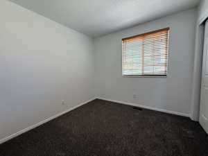 Neutral interior room featuring a window with wood-finish blinds, textured dark carpeting, and light-toned walls