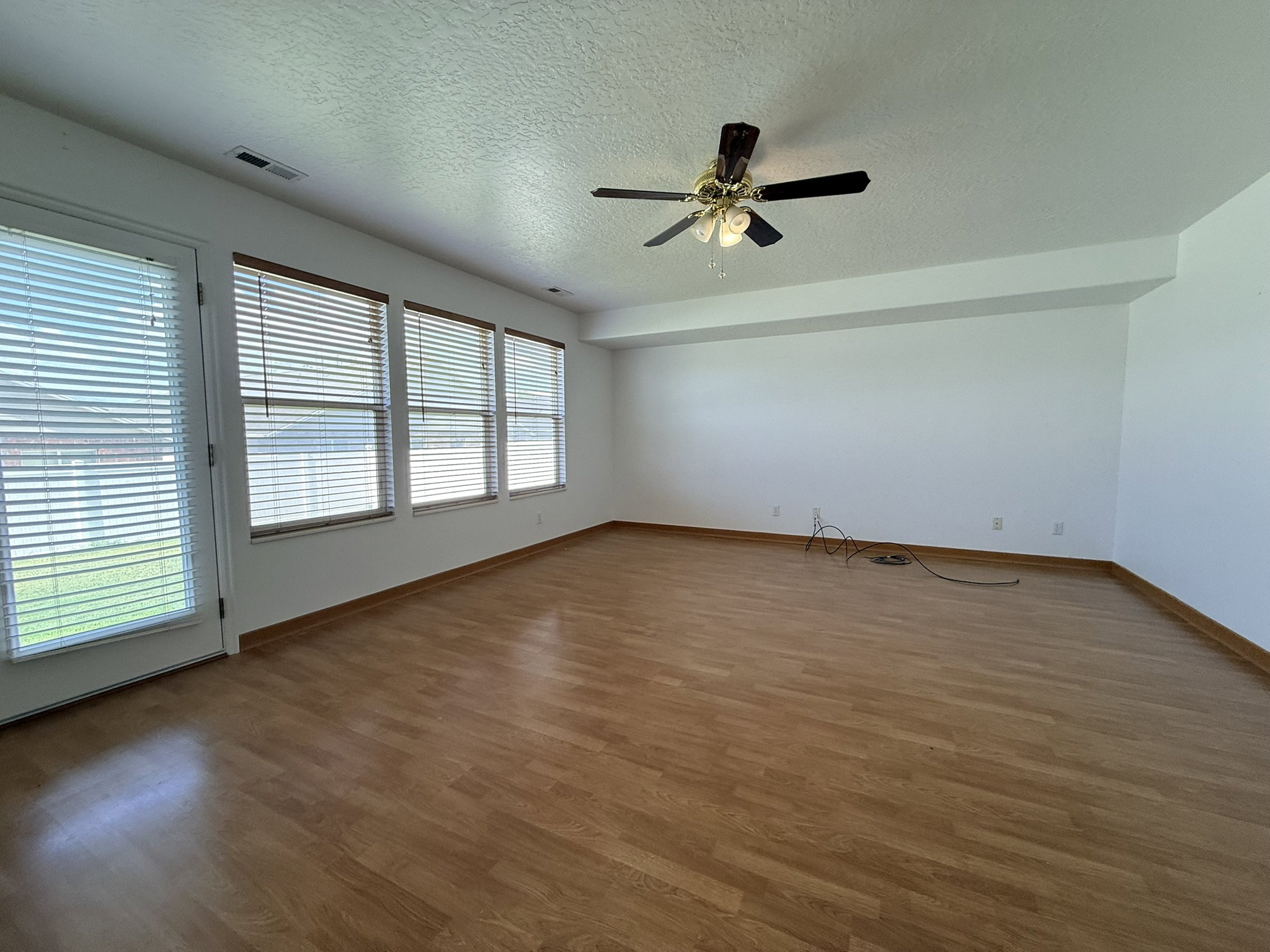Spacious interior featuring wood-finish flooring, a ceiling fan with integrated lighting, multiple windows with blinds, and a white color palette