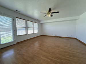 Spacious interior featuring wood-finish flooring, a ceiling fan with integrated lighting, multiple windows with blinds, and a white color palette