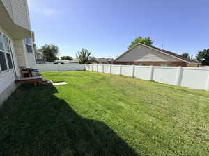 Expansive backyard featuring a lush lawn, complete white vinyl fencing, a partial wooden deck with steps, and a bay window on the home's exterior