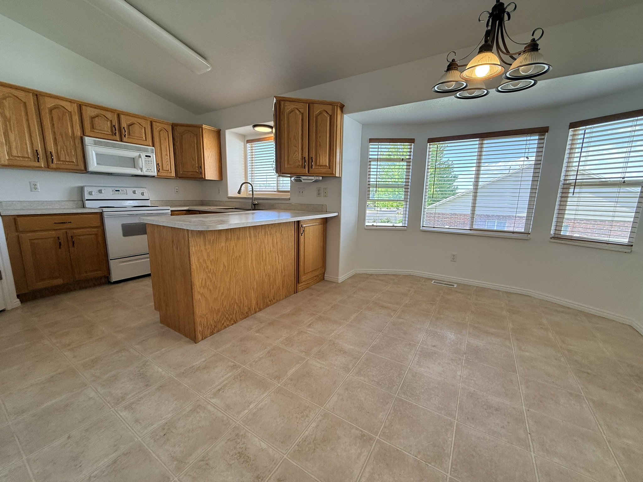 Kitchen area featuring wood cabinetry, white appliances, a center island with countertop seating, and tile flooring